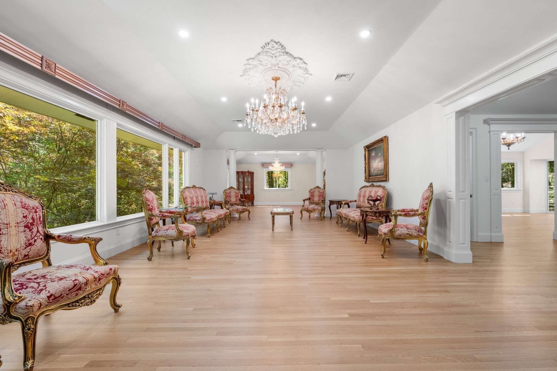 Formal sitting room with ornate pink chairs, pale wood floors, and a crystal chandelier.