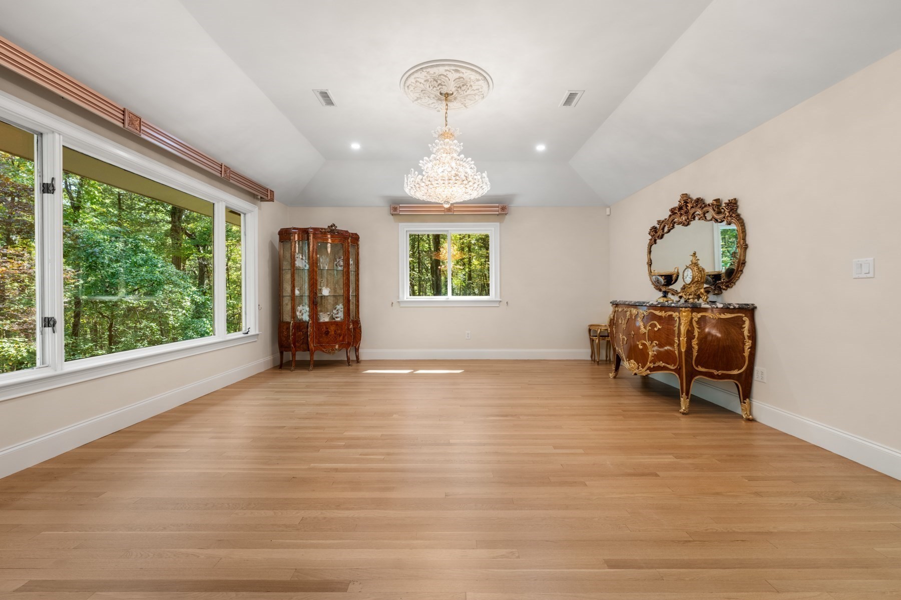 Dining room with a crystal chandelier, hardwood floors, and windows overlooking leafy trees.