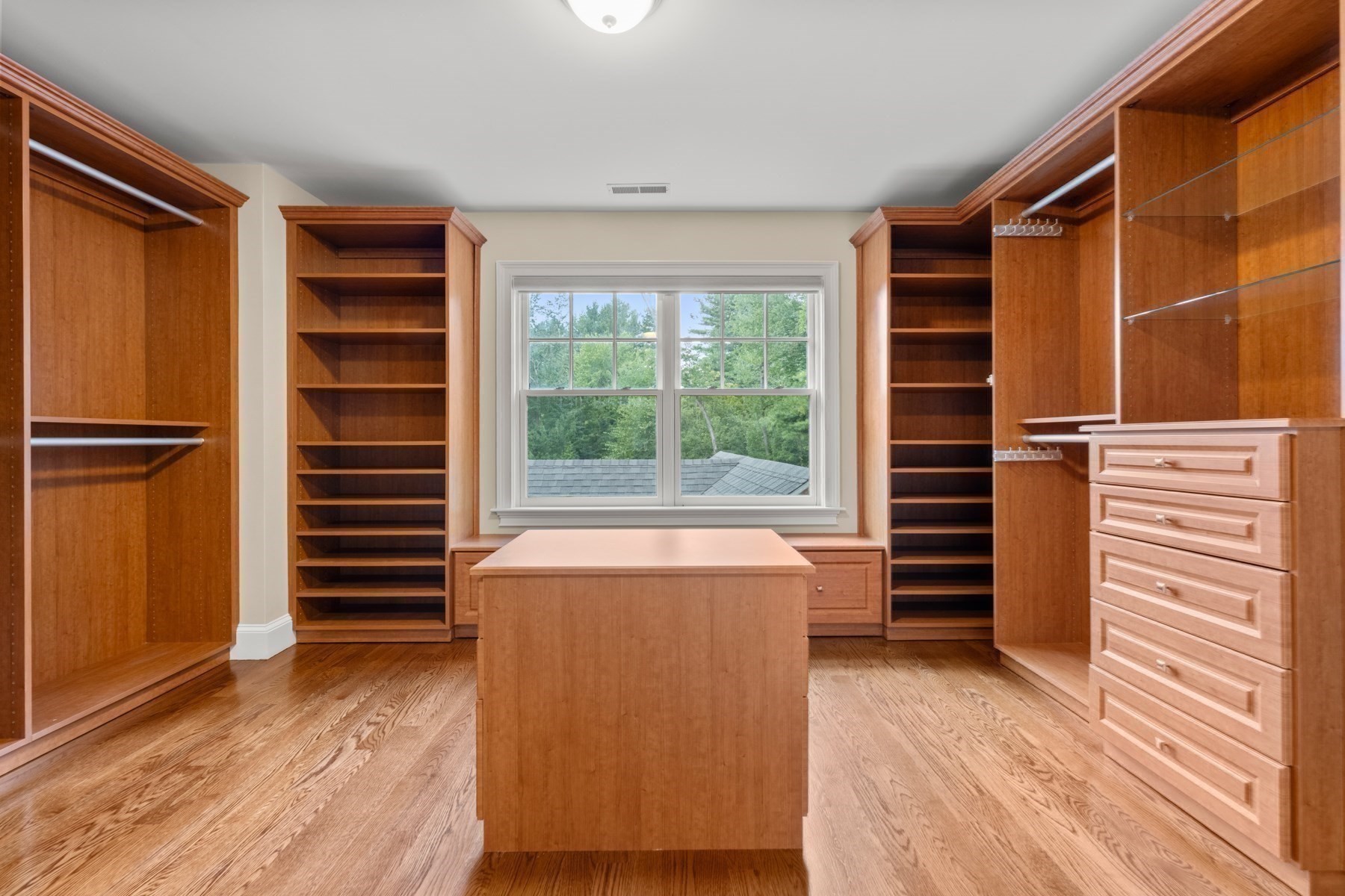 Walk-in closet with wood built-ins, a central island, and a large window overlooking trees.