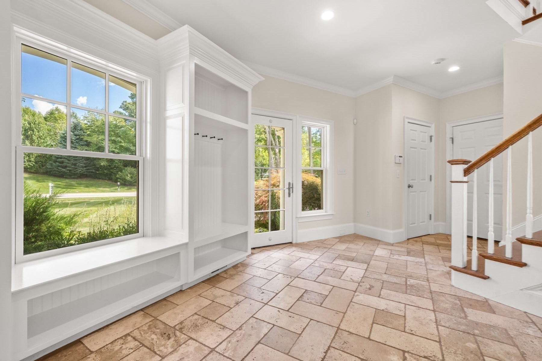 Bright entry foyer with built-in bench, stone tile floor, and staircase beside a large window.