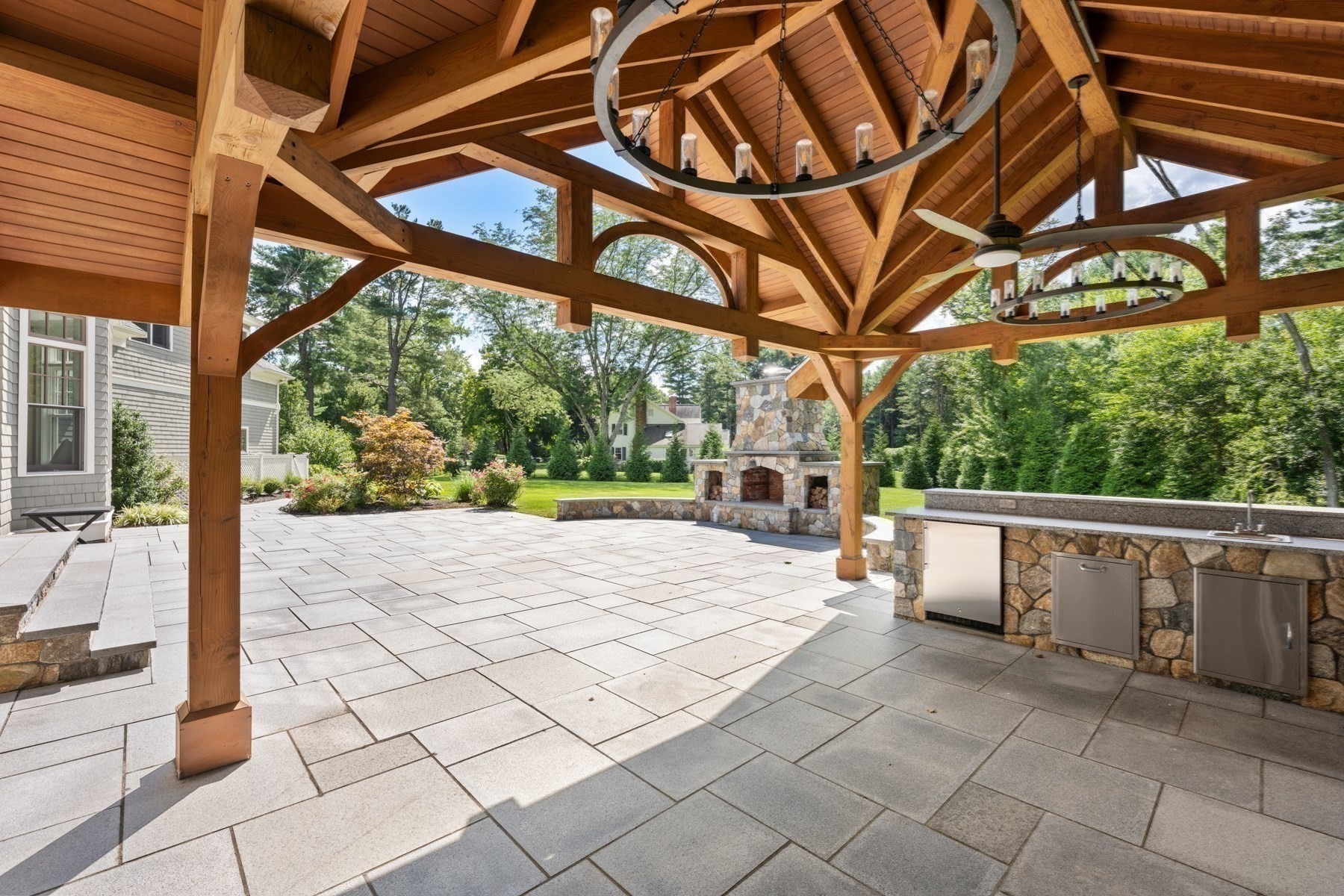 Stone patio beneath a timber pavilion, with a large fireplace and built-in outdoor kitchen.