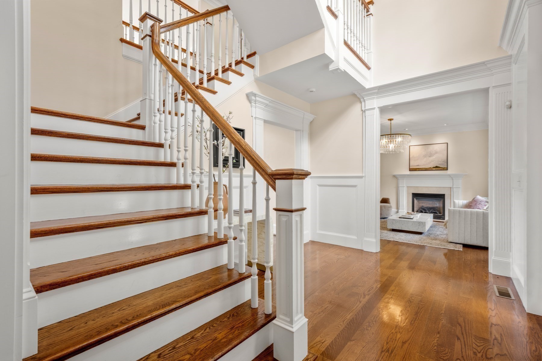 Foyer with a sweeping wood-and-white staircase and a view into the fireplace living room.