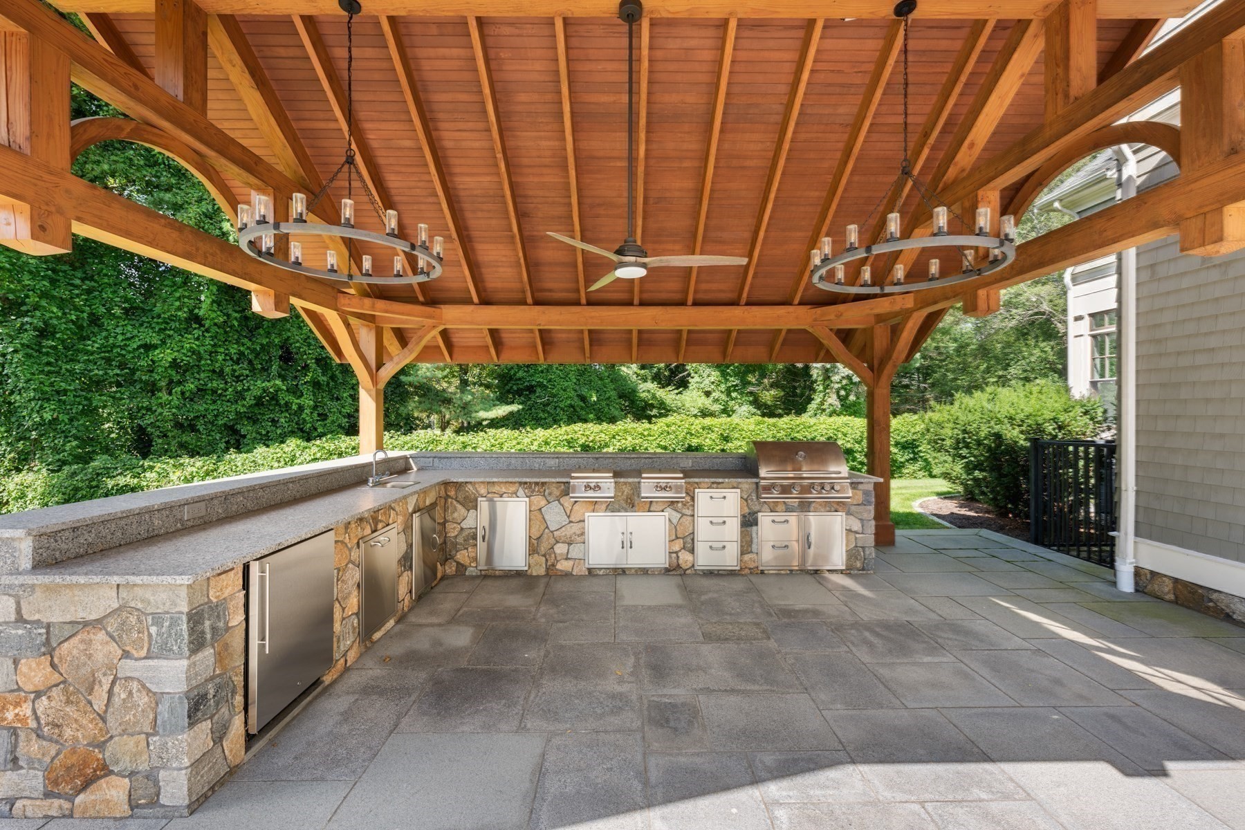 Covered outdoor kitchen with a timber pavilion, stone counters, stainless-steel appliances, and built-in grill.