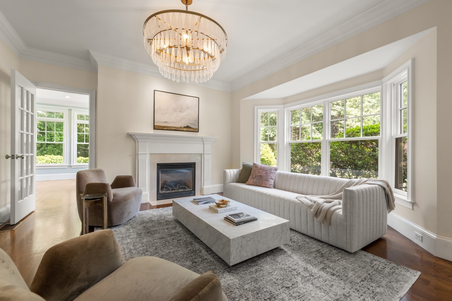 Living room with a white fireplace, bay windows, crystal chandelier, and marble coffee table.