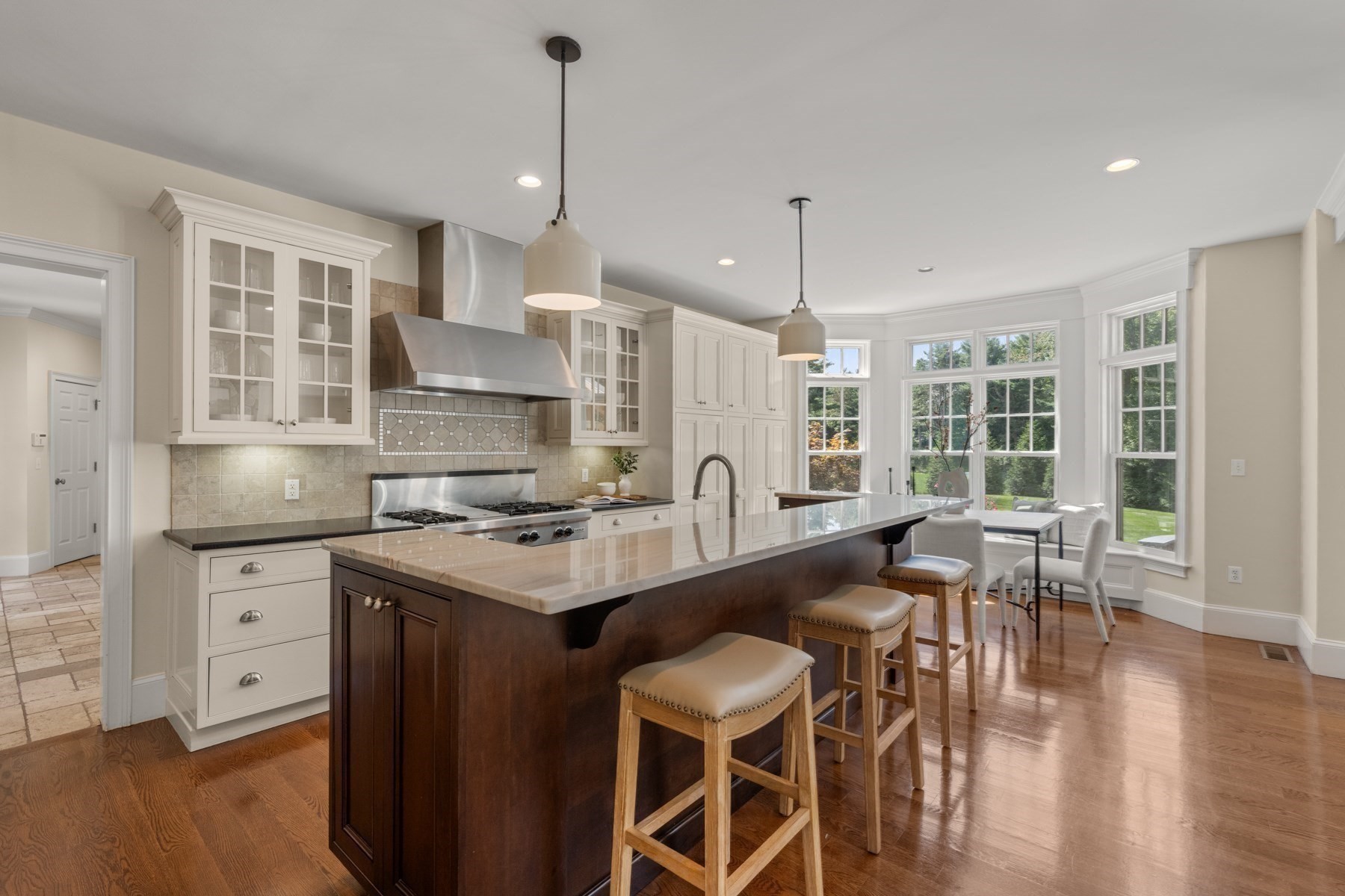 Bright kitchen with a large island, bar stools, white cabinetry, and a window-side dining nook.