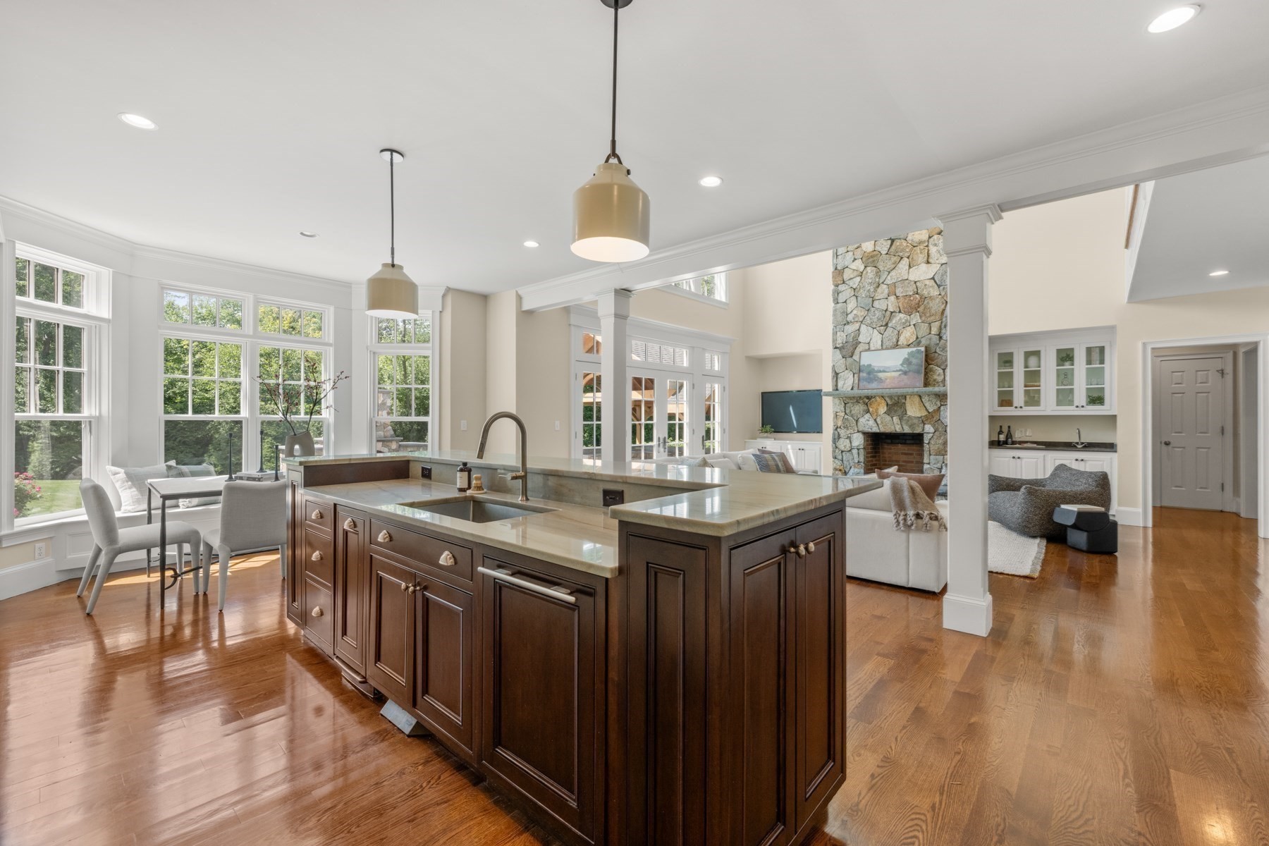 Open kitchen with a large dark wood island, tall windows, and an adjoining living room with a stone fireplace.