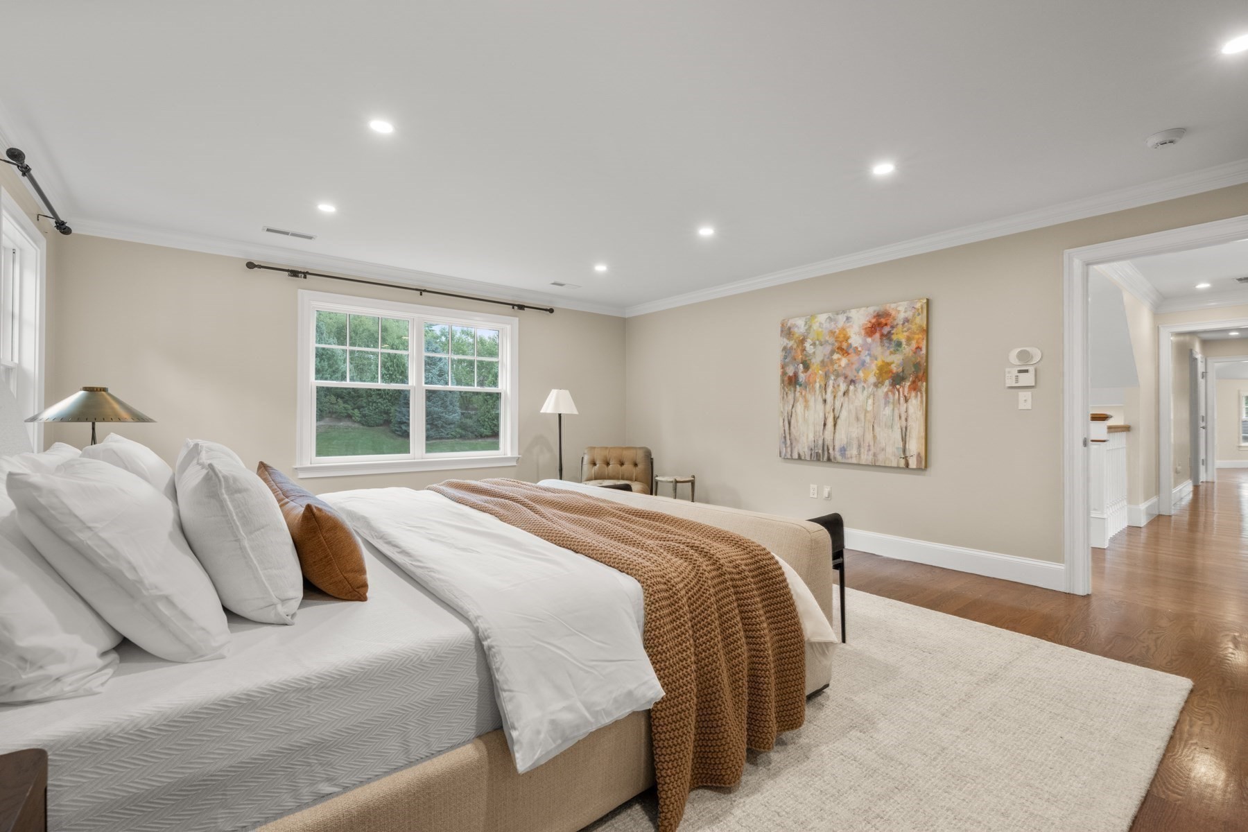 Furnished bedroom with a large white bed, brown knit throw, and window overlooking greenery.