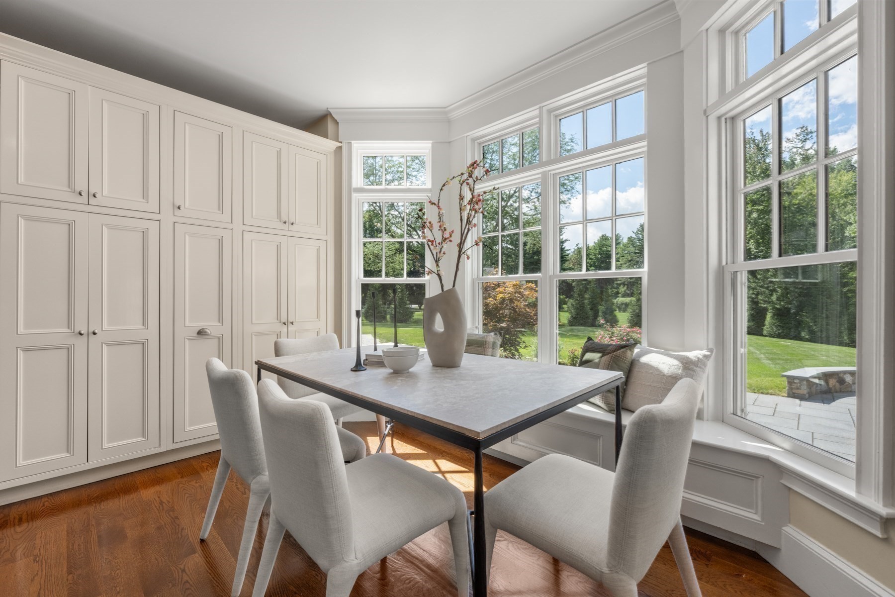 Dining room with white paneled cabinets, a dining table, and tall windows overlooking the garden.