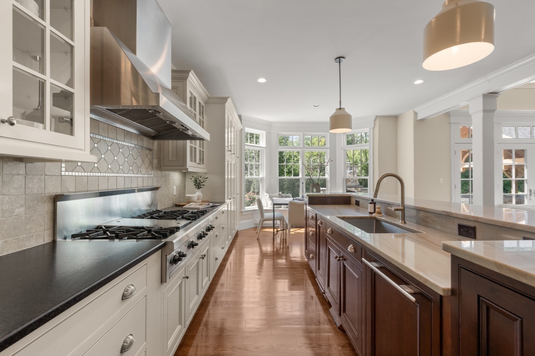 Kitchen with a large island, professional gas range, and sunny breakfast nook beside tall windows.
