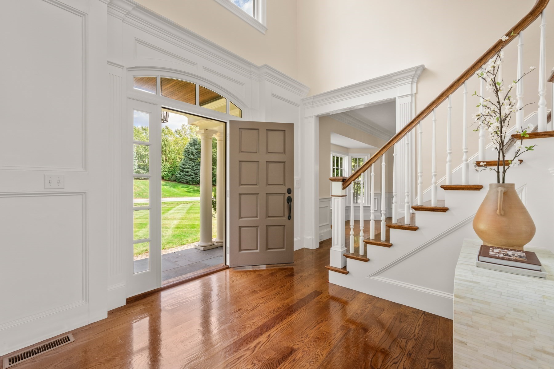 Front entry foyer with polished hardwood floors, an open door, and a white staircase with a wood handrail.