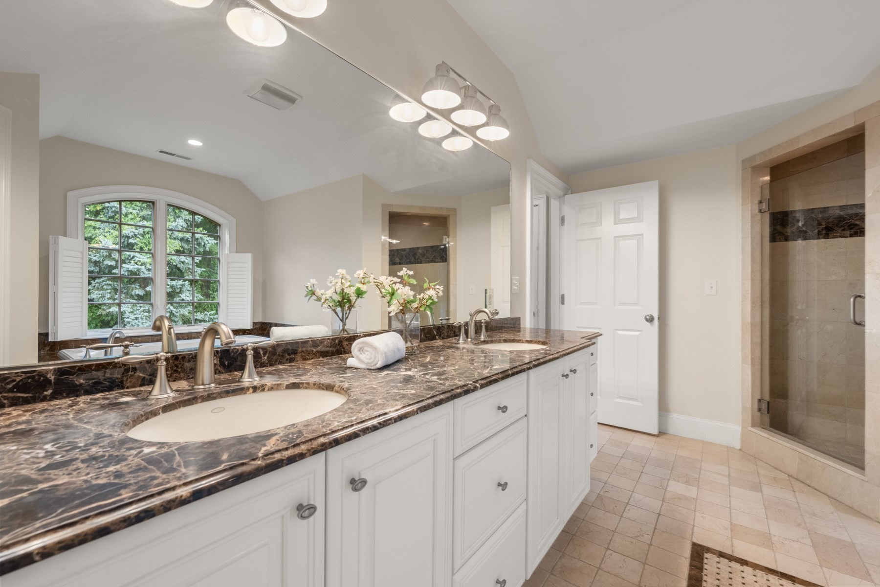 Bathroom with a double vanity, dark marble countertop, arched window, and glass-enclosed shower.
