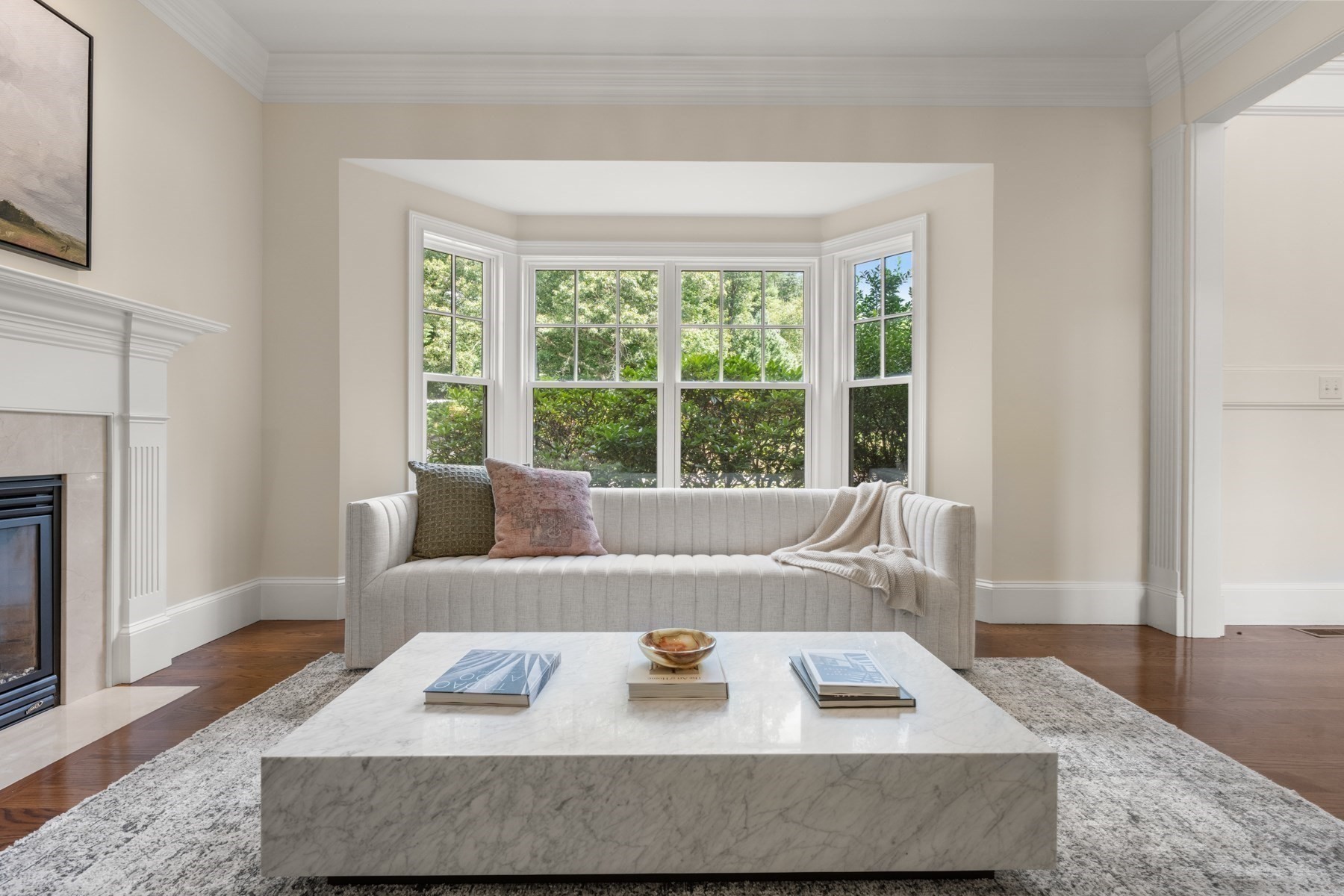 Living room with bay windows, a light sofa, marble coffee table, and fireplace.