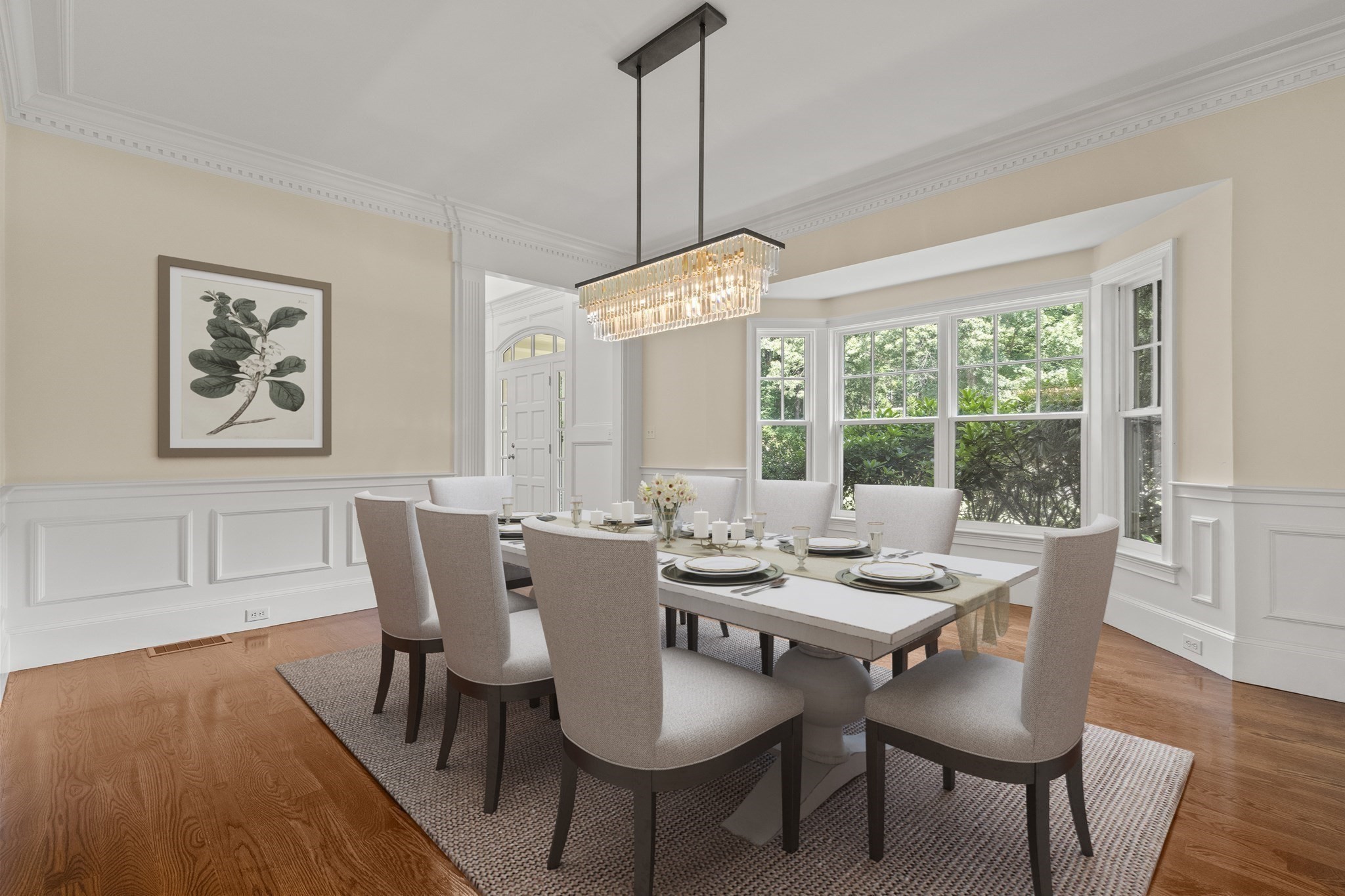 Dining room with a set table, crystal chandelier, and bay windows overlooking greenery.