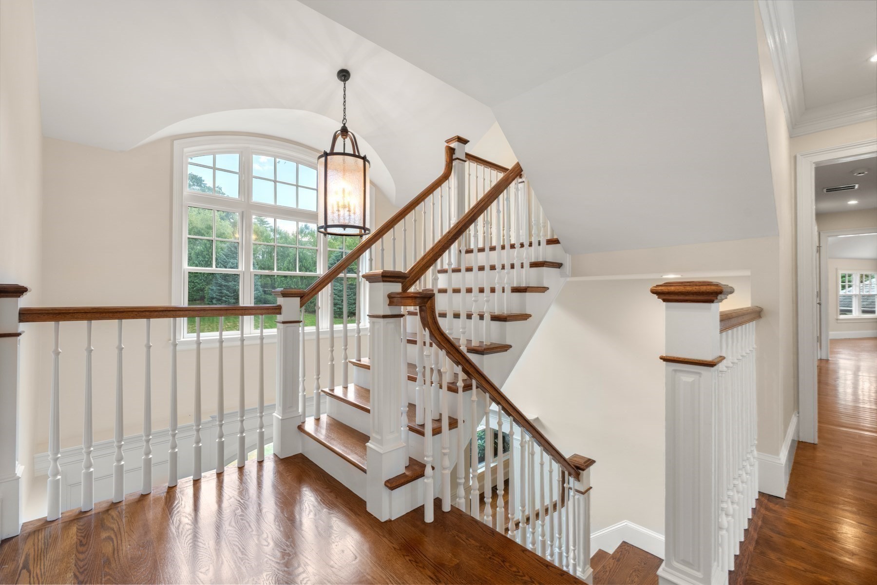 Staircase with white balusters, wood handrails, polished hardwood floors, and a large arched window.