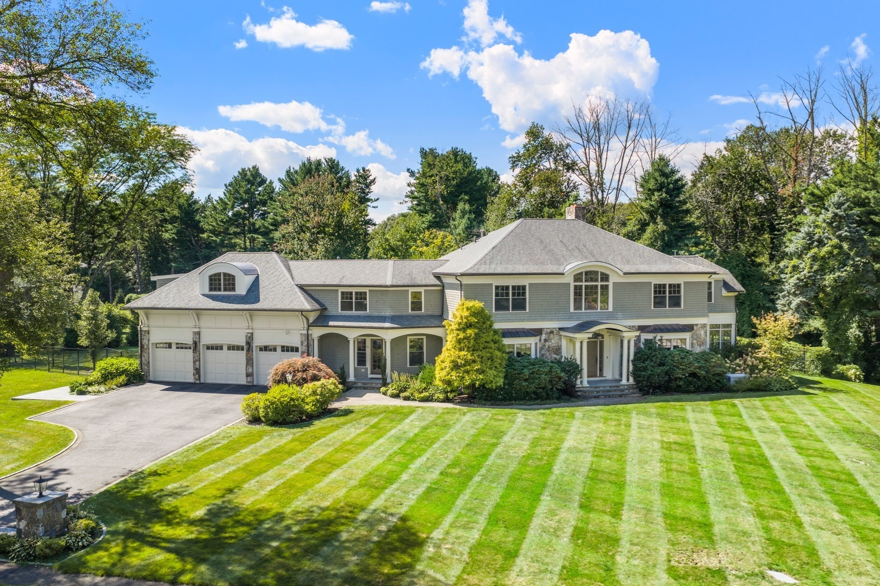 Large gray-shingled house with stone accents, three-car garage, and a broad striped lawn.