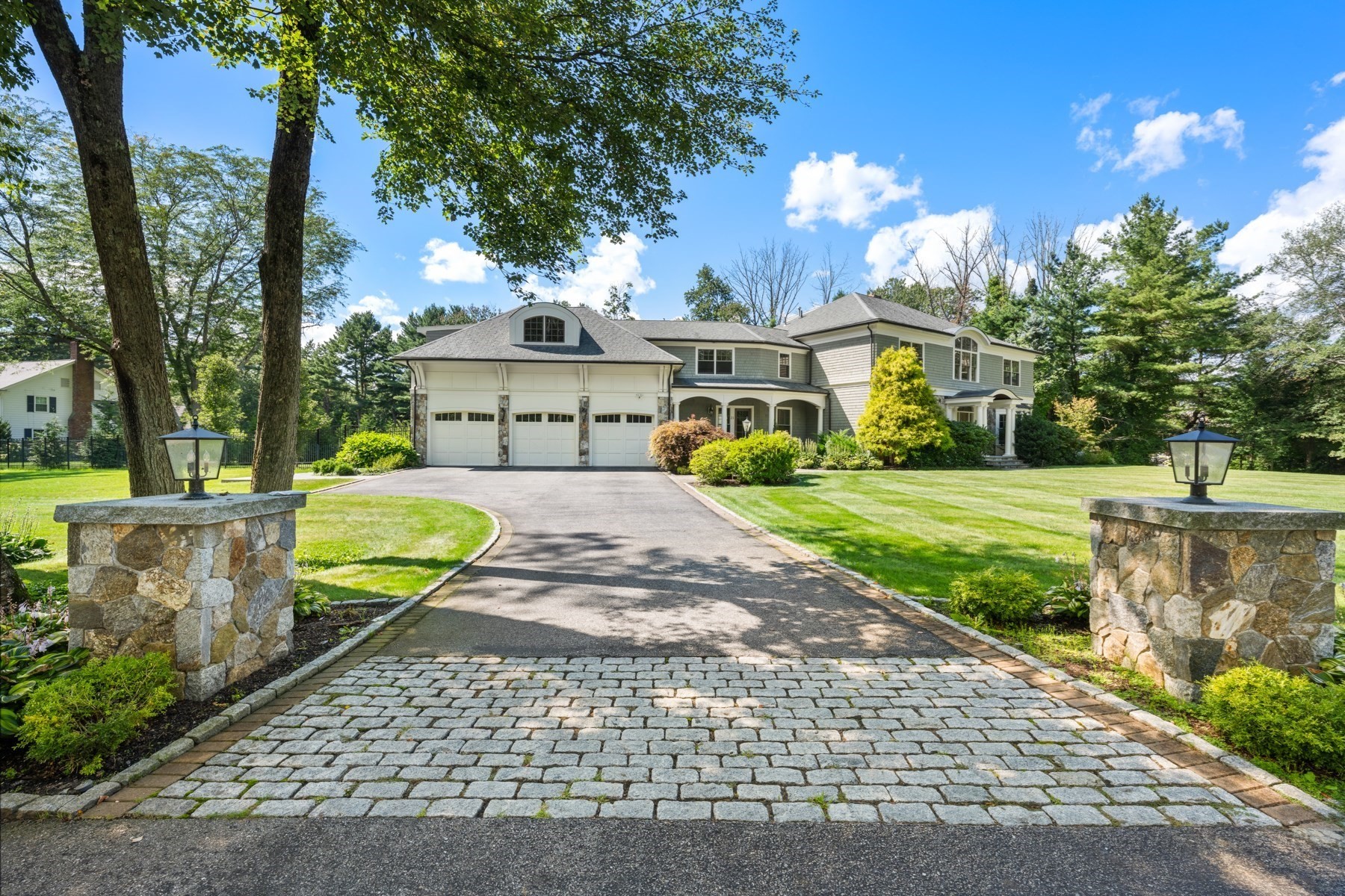 Large two-story home with a three-car garage beyond a cobblestone driveway and stone entrance pillars.