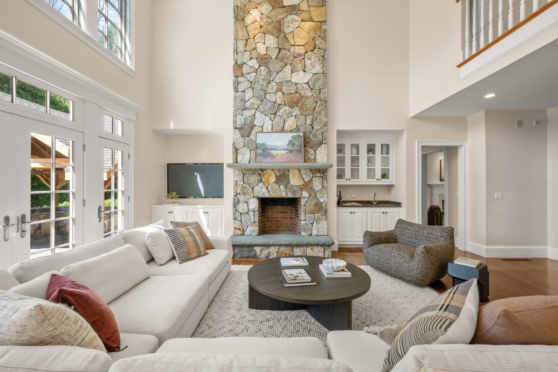 Living room with a soaring stone fireplace, white sofas, and tall windows.