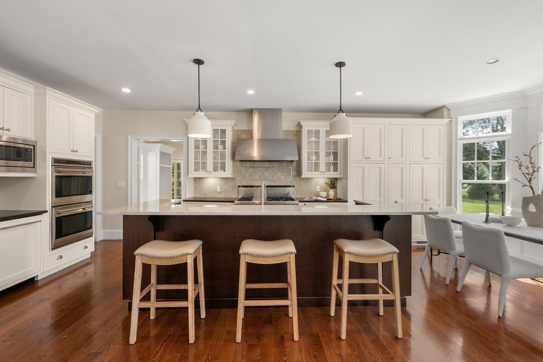 Kitchen with white cabinetry, a large dark island, three bar stools, and an adjoining dining area.