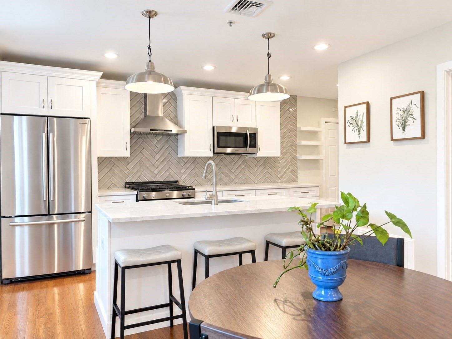 Modern kitchen with a herringbone backsplash, stainless appliances, marble island, and dining table.
