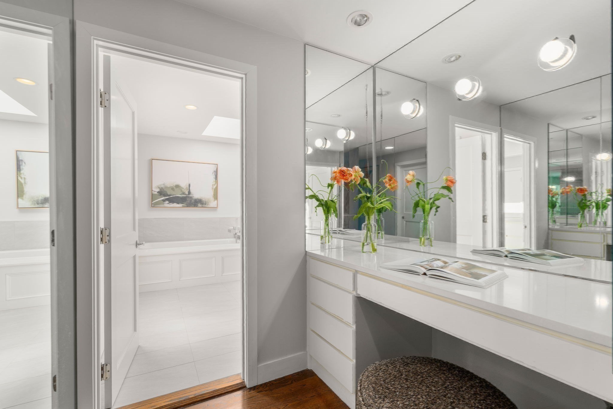 Bright bathroom vanity with mirrored walls and orange flowers beside a white soaking tub.