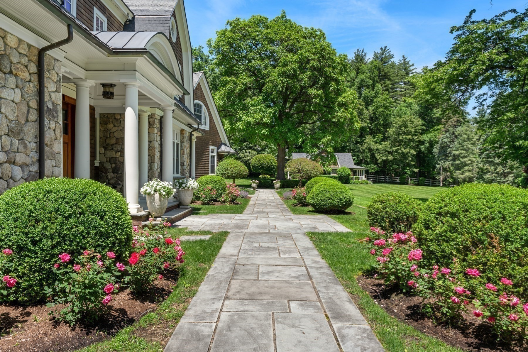 Home with a stone facade and columned entrance beside a rose-lined stone walkway.
