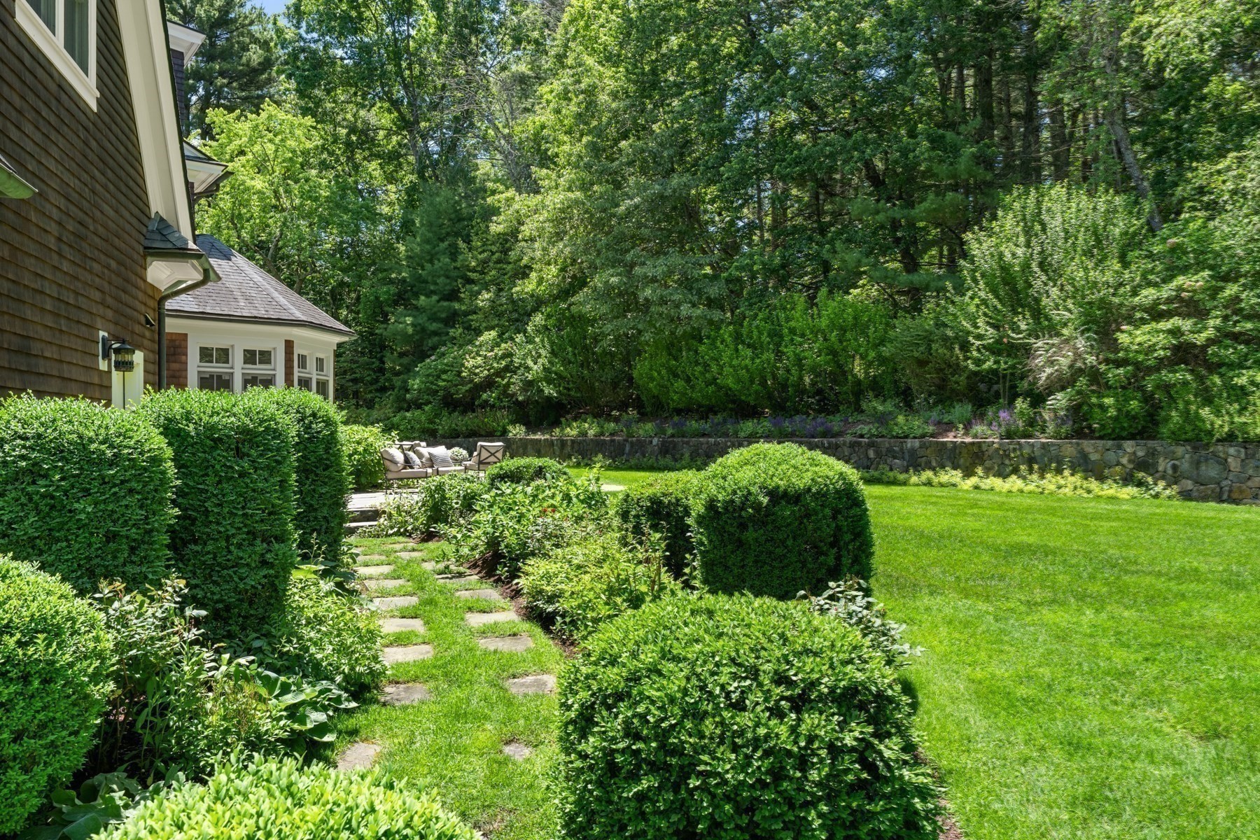 Landscaped backyard with a stone garden path, patio seating, and mature trees.