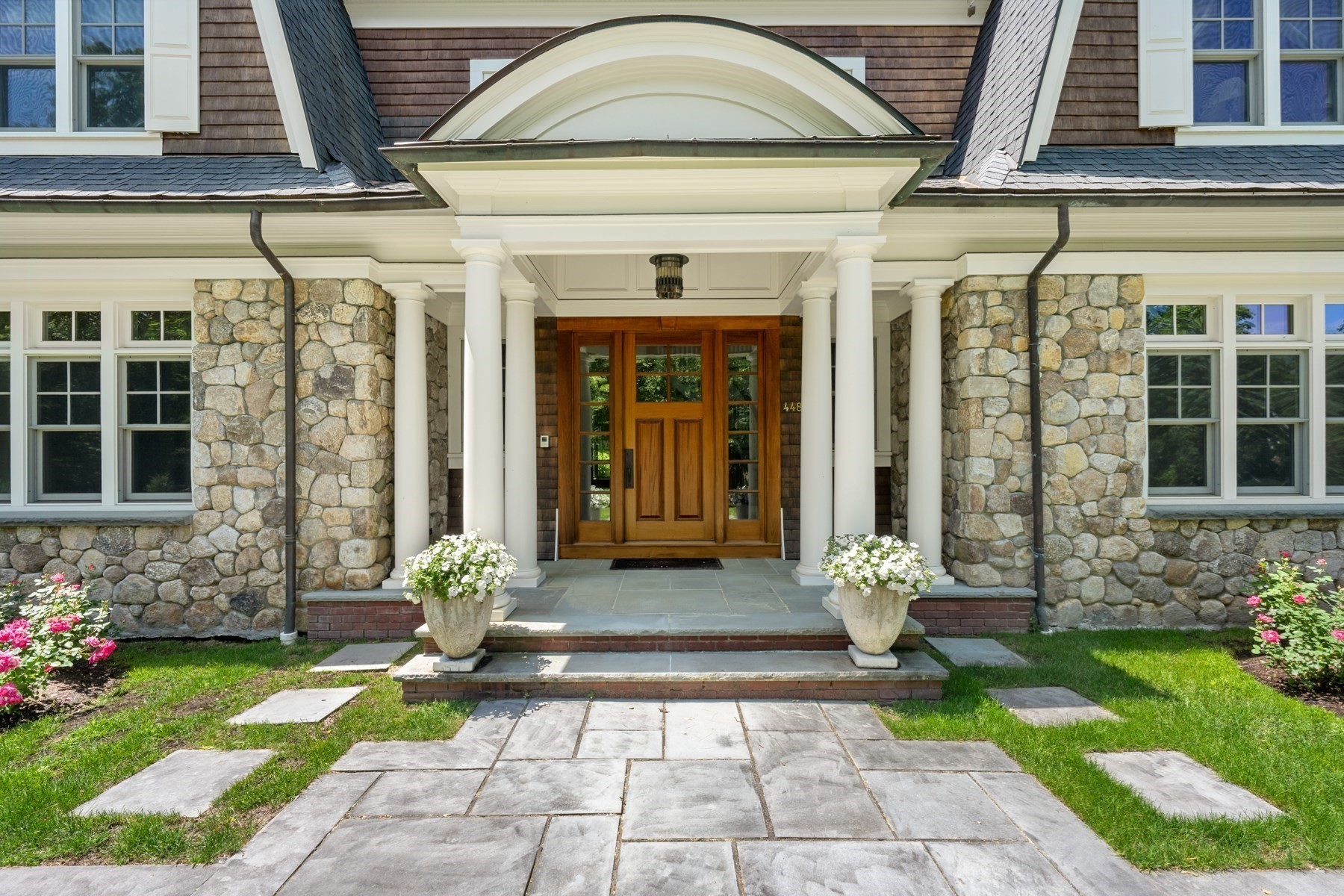 Home entrance with a columned portico, stone facade, wood door, and flower planters.