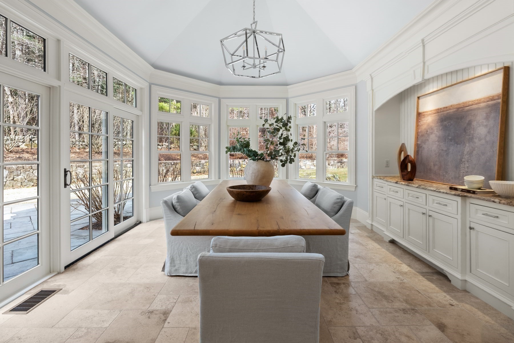 Bright dining room with a long wooden table, white built-ins, and expansive windows overlooking the yard.