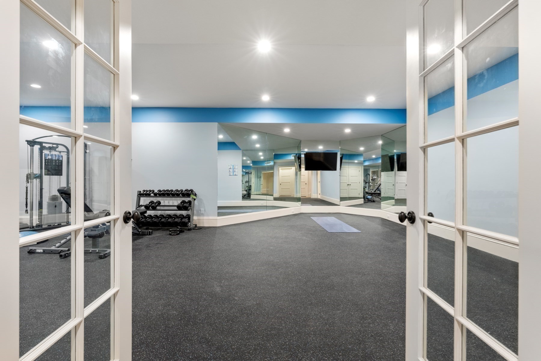 Home gym with mirrored walls, dumbbells, strength equipment, and a yoga mat.