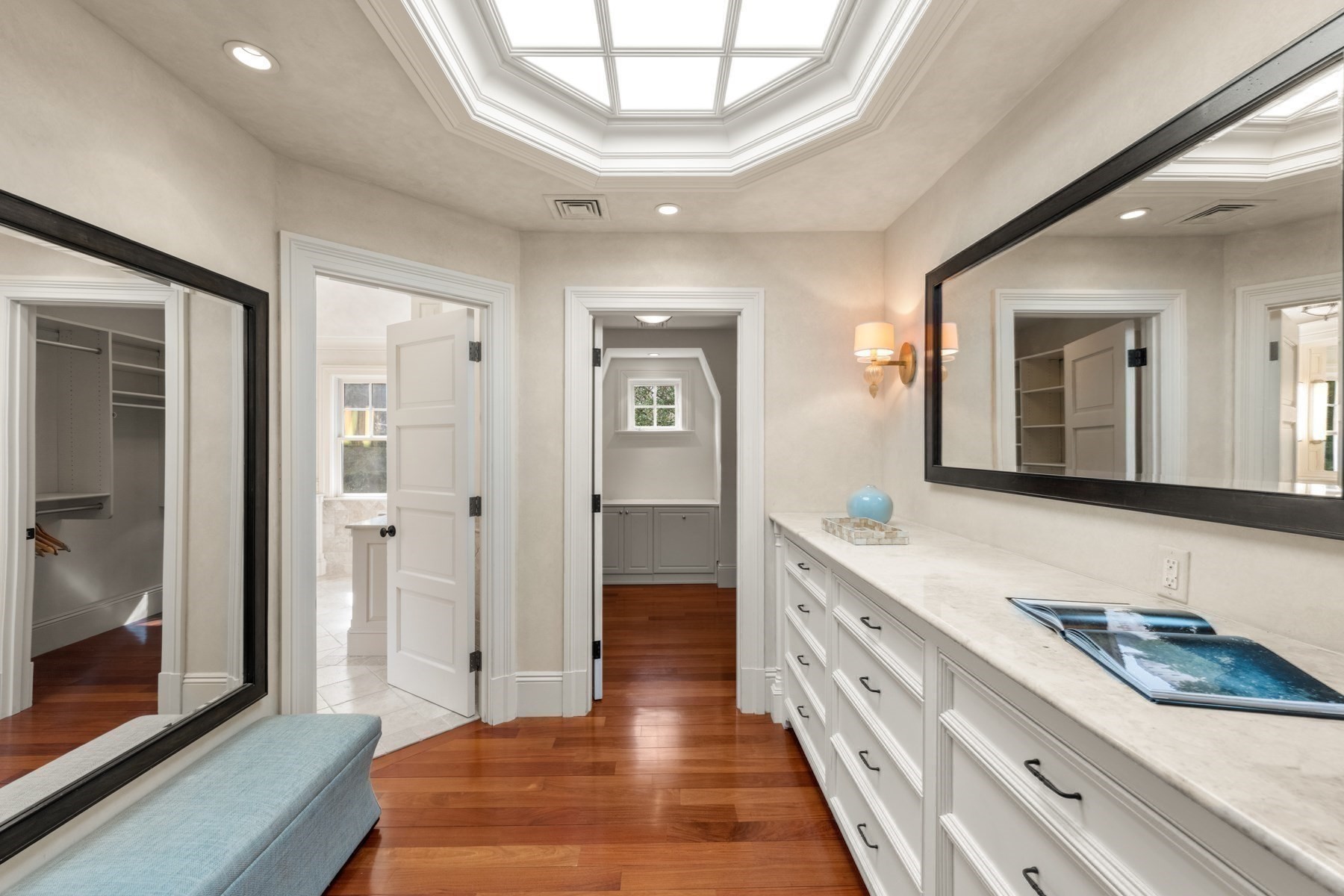 Dressing room with a long white vanity, large mirror, skylight, and blue upholstered bench.