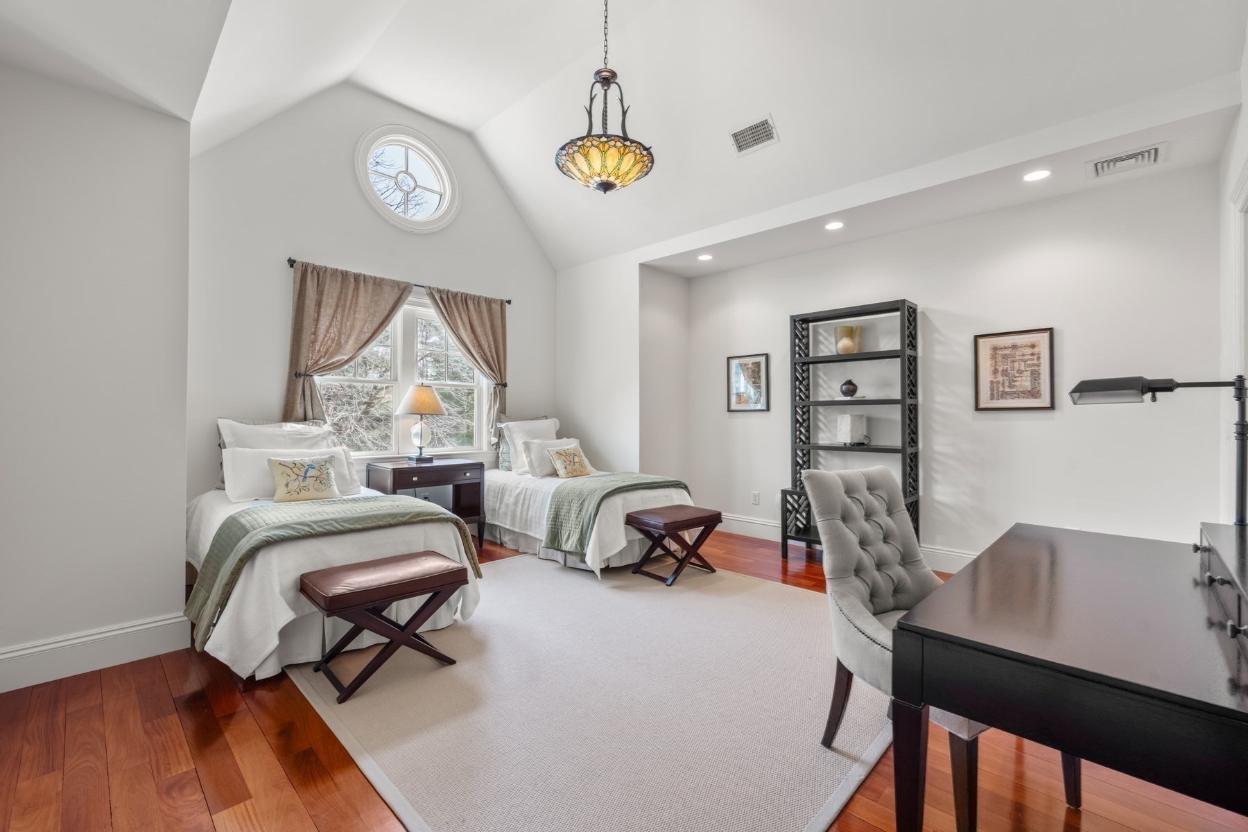 Bedroom with twin beds, a vaulted ceiling, and a round window above the curtains.