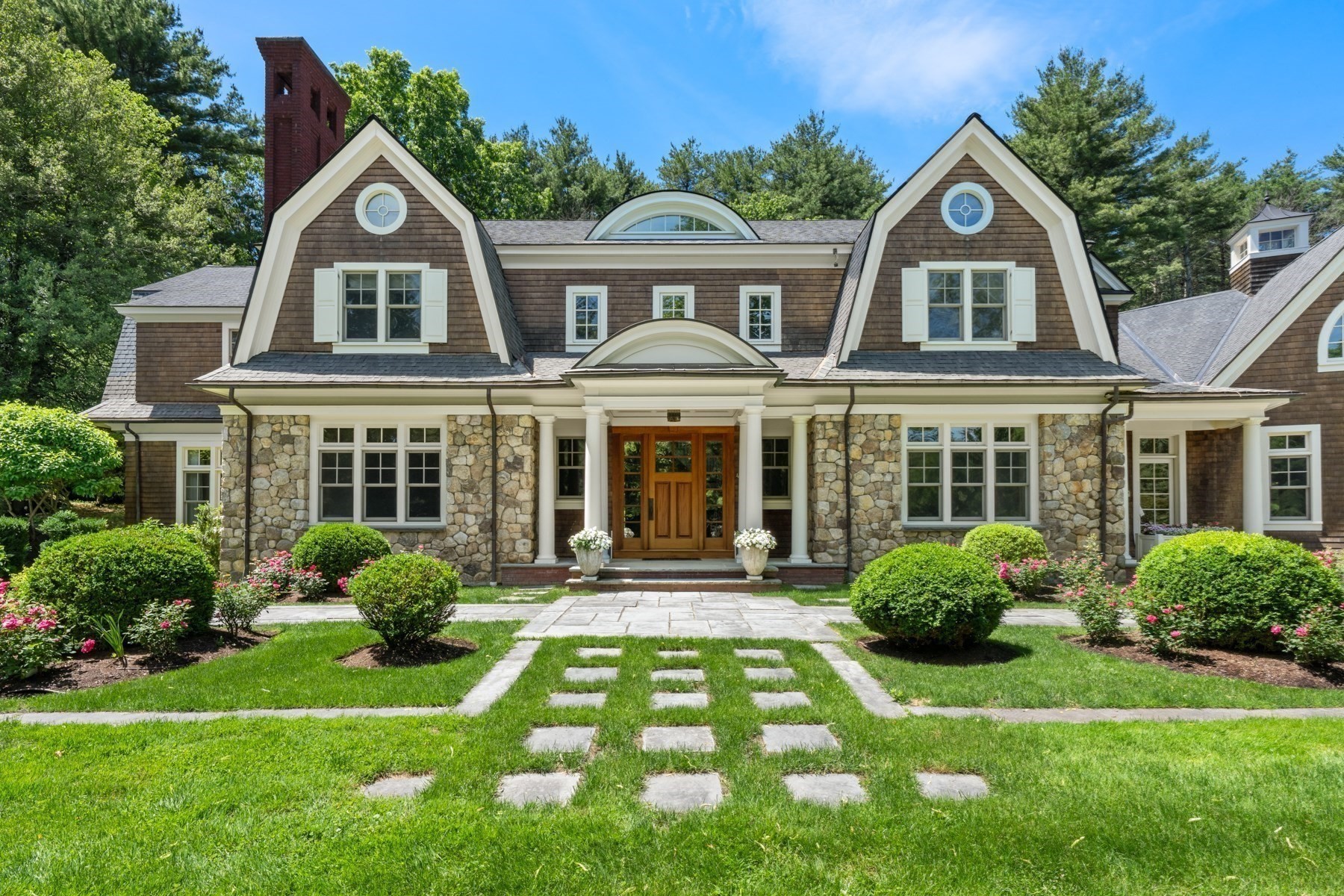 Home with stone facade, twin shingled gables, and a landscaped front lawn.