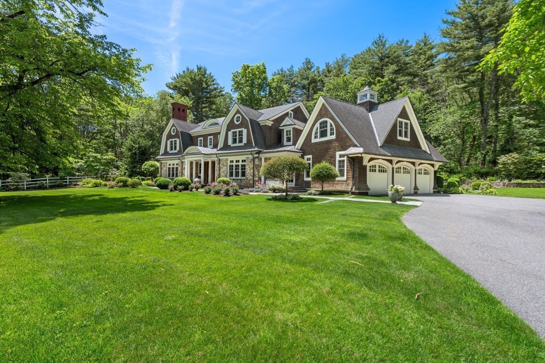 Shingle-style home with stone accents, three garage doors, and a broad landscaped lawn.