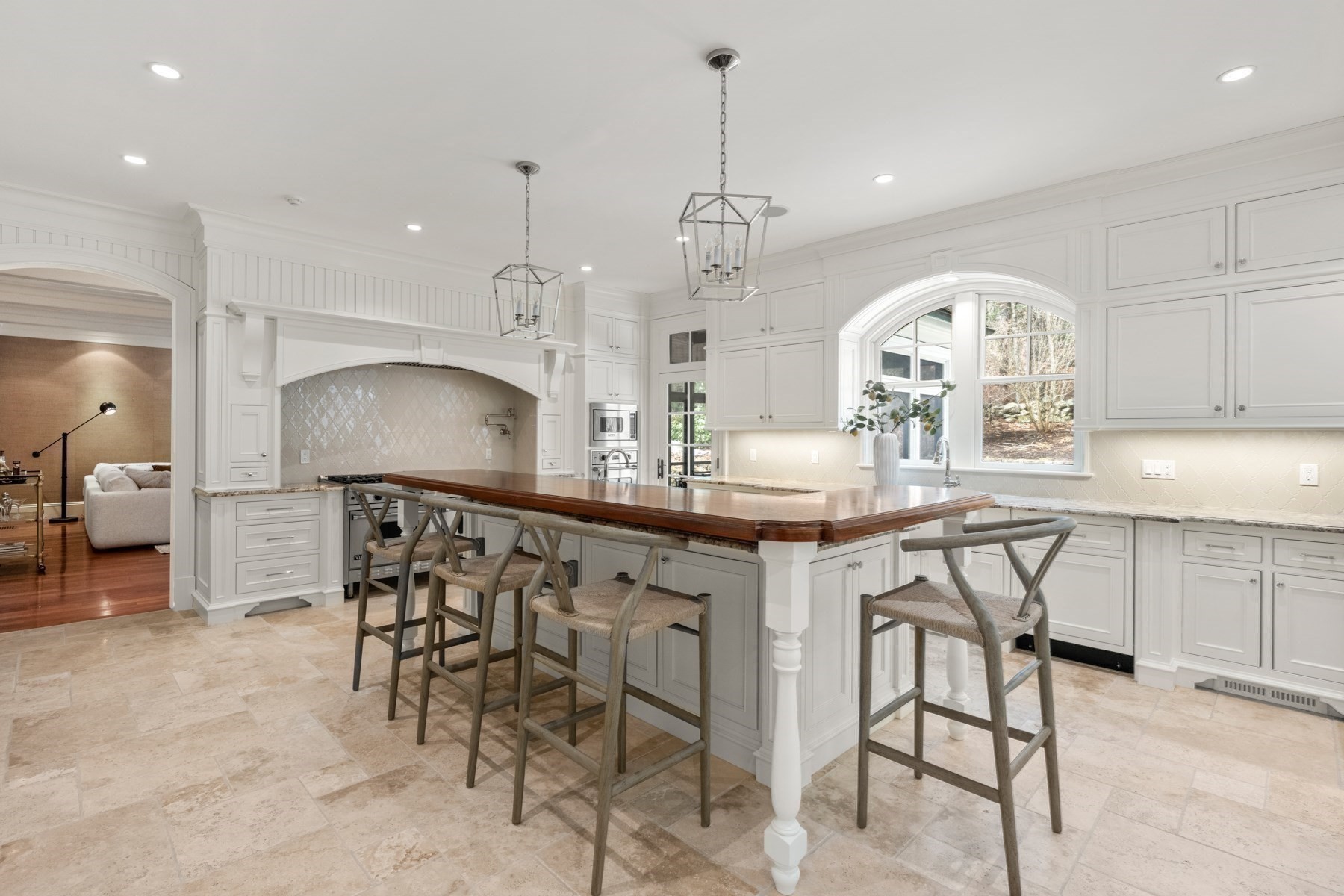 White kitchen with a wood-topped island, bar stools, and an arched window above the sink.