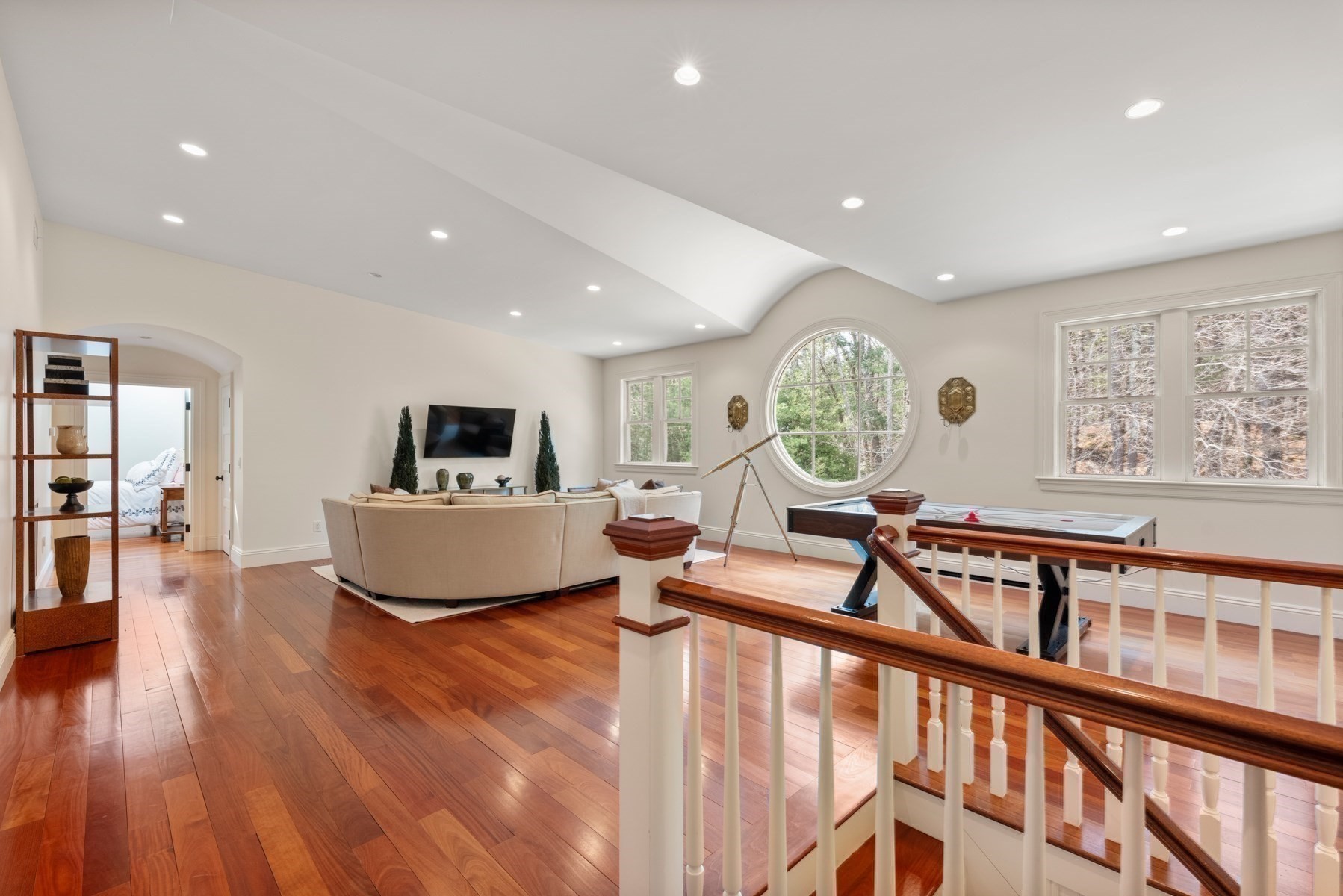 Living room with a round picture window, beige sectional, hardwood floors, and a pool table.
