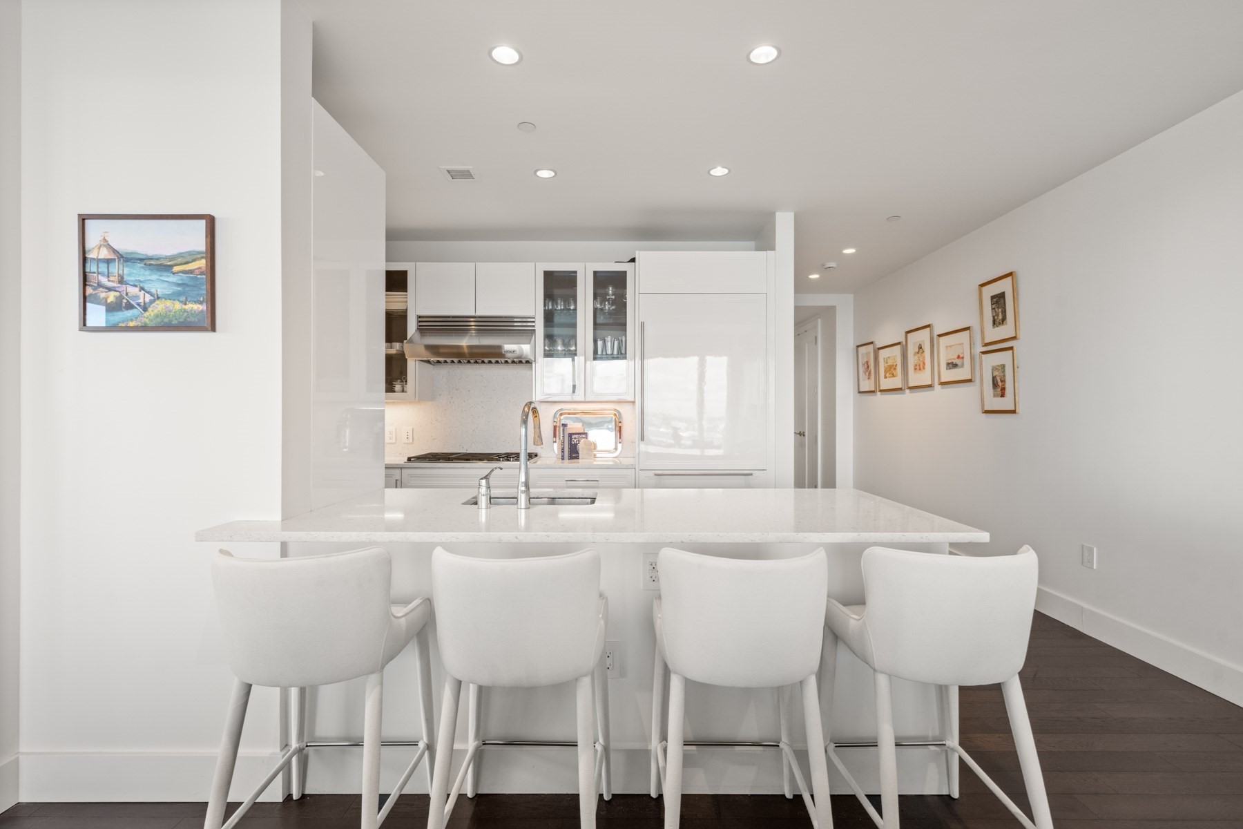 Modern white kitchen with a large island and four white bar chairs.