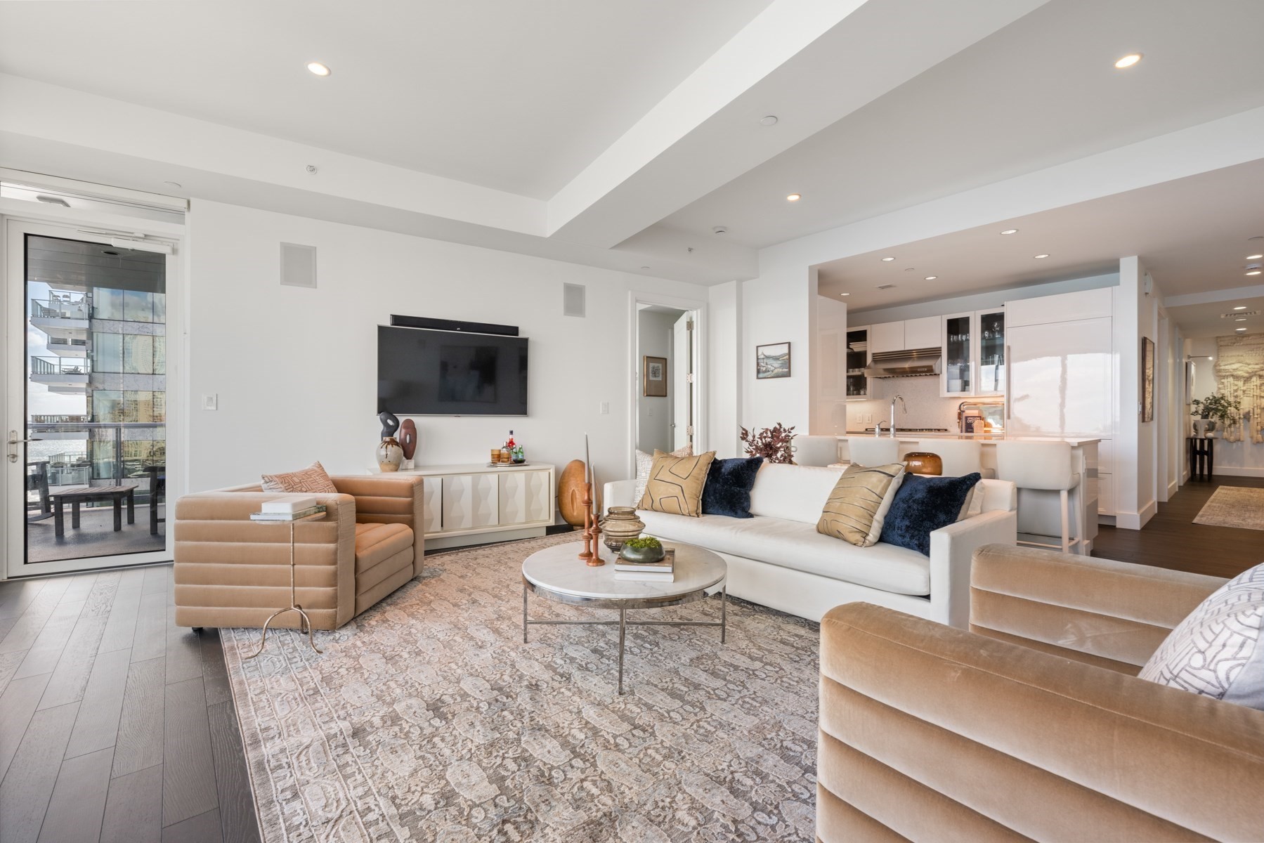Furnished living room with white sofa, patterned rug, open kitchen, and sliding doors to a balcony.
