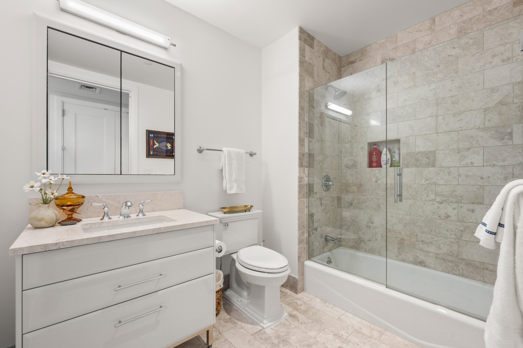 Bathroom with a white vanity and mirrored cabinet beside a glass-enclosed tub and tiled shower.
