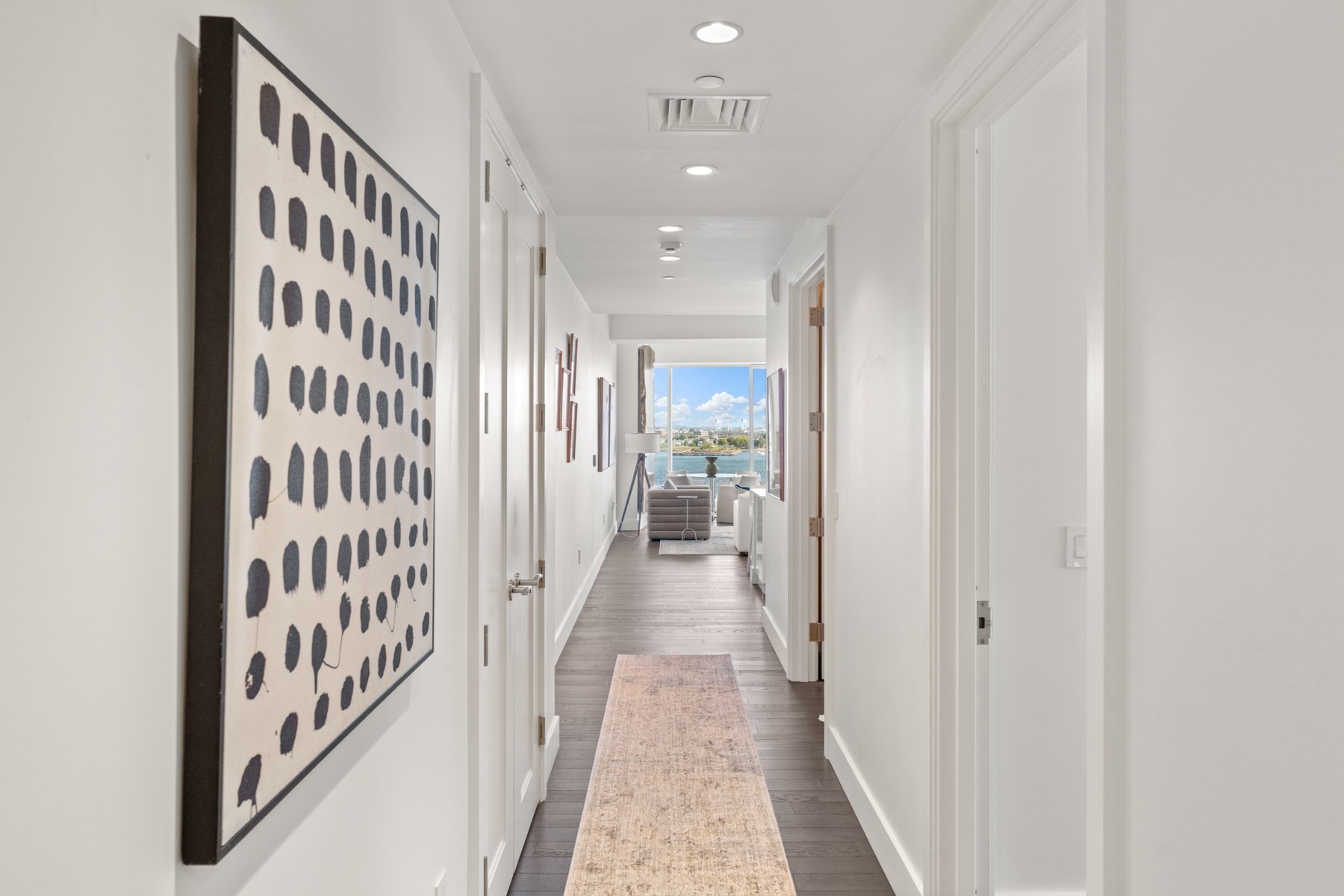 Bright apartment hallway with a patterned runner leading to a waterfront living room.