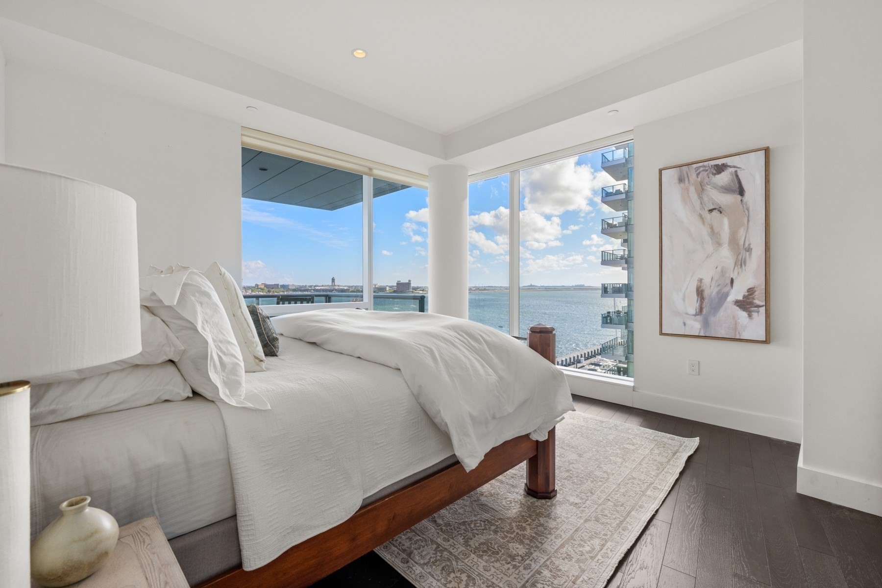 Bedroom with white bedding and corner windows overlooking the water.