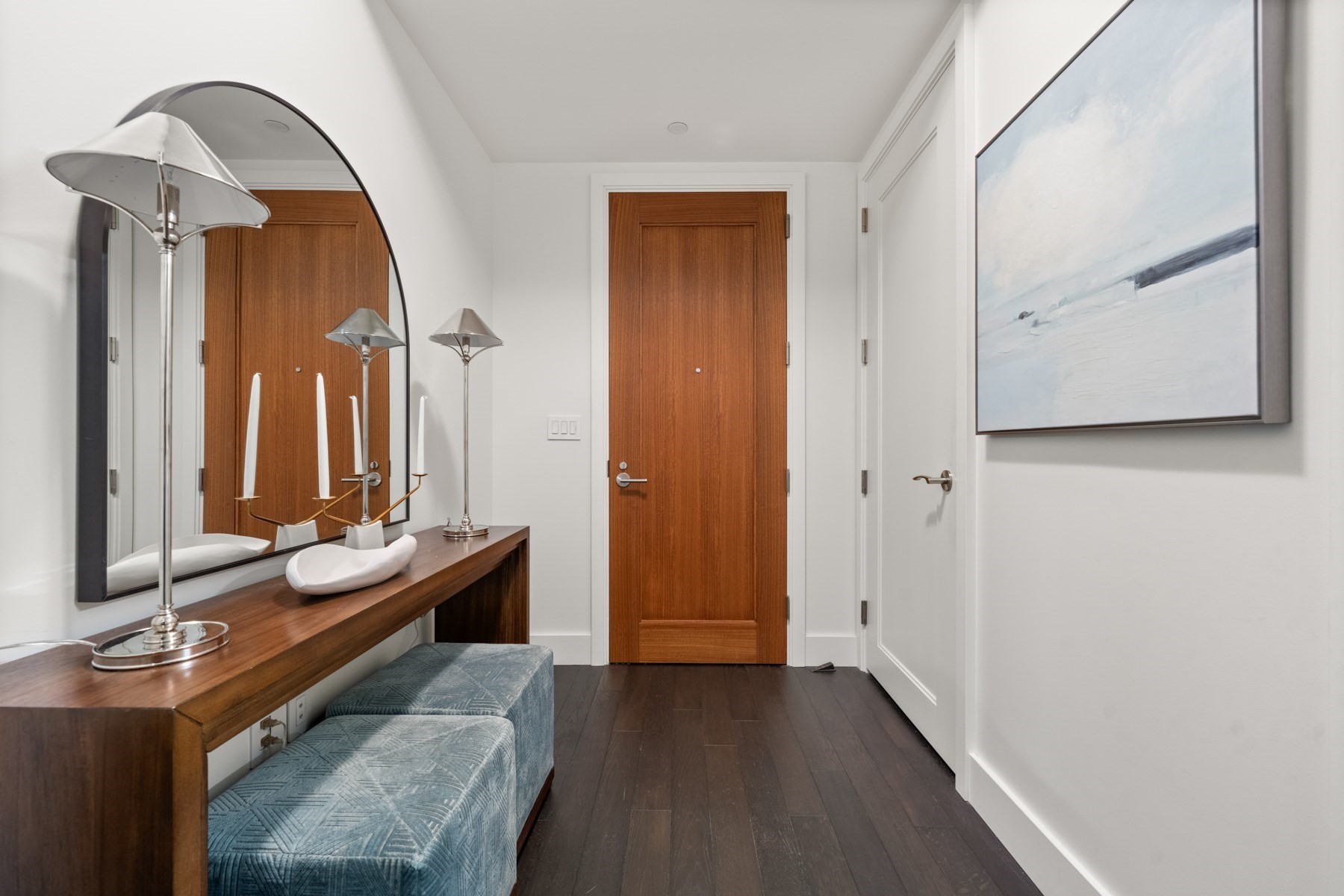 Apartment entry hall with a wood console, arched mirror, and blue upholstered bench.