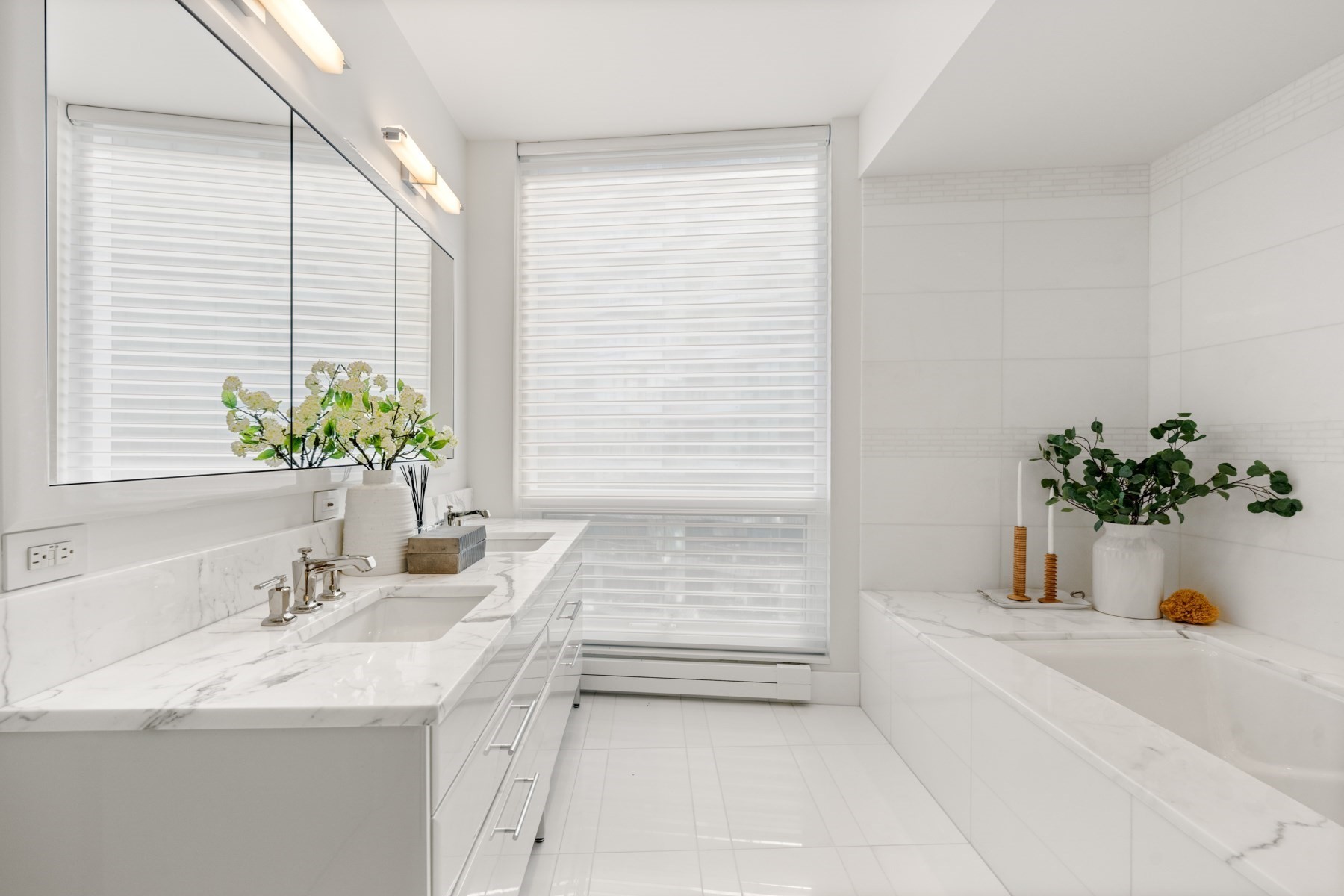 Bright white bathroom with a marble double vanity, large mirror, and bathtub.
