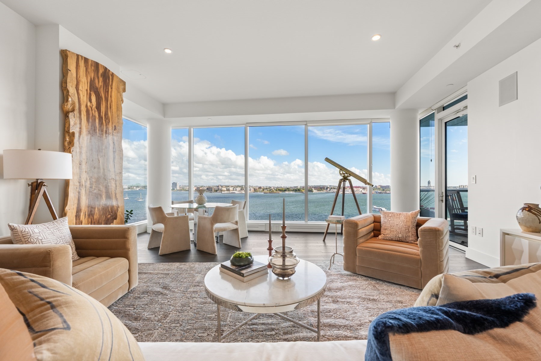 Furnished living room with floor-to-ceiling harbor views, a telescope, and a dramatic natural wood slab.