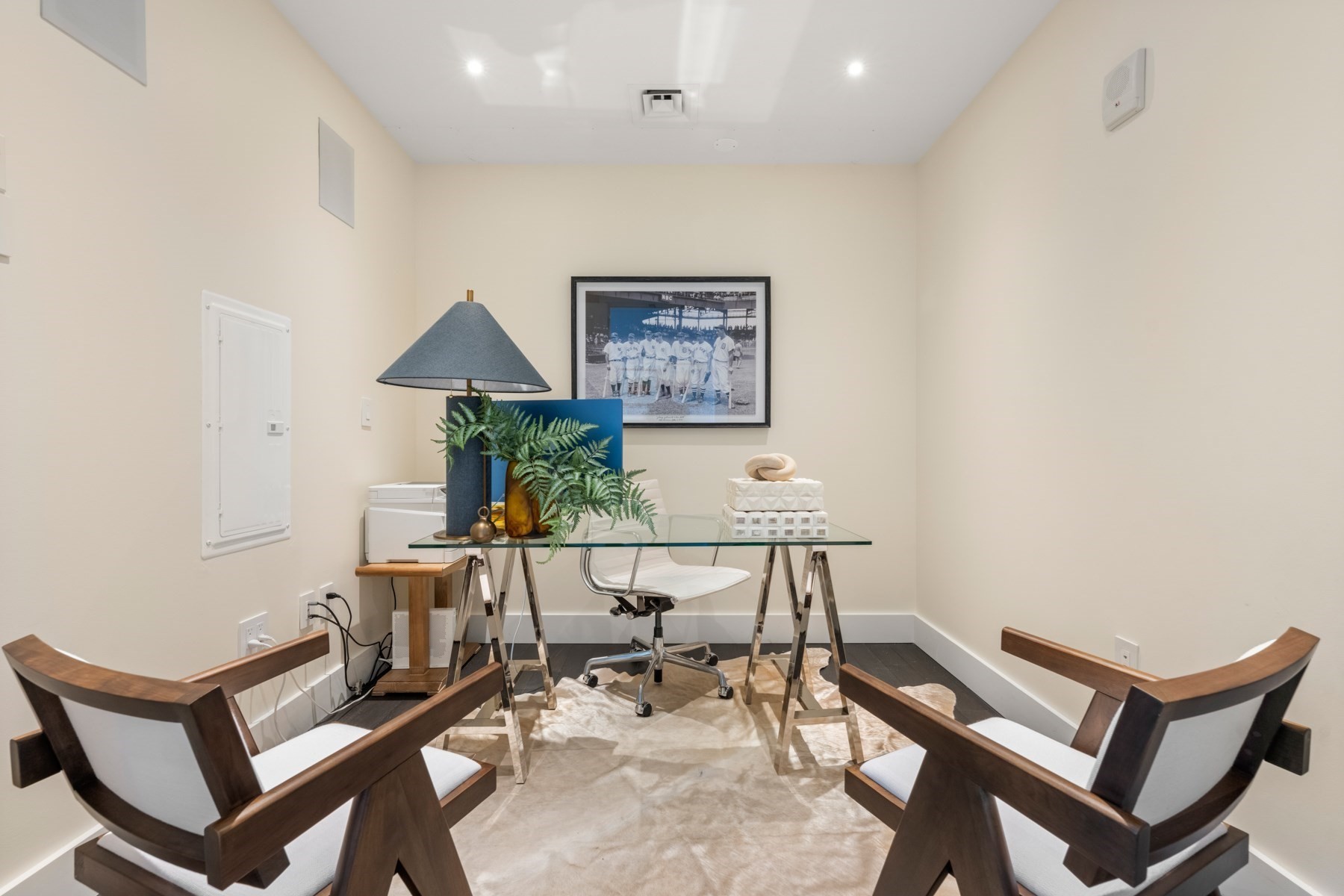 Furnished home office with a glass desk, two wood guest chairs, and a framed baseball photograph.