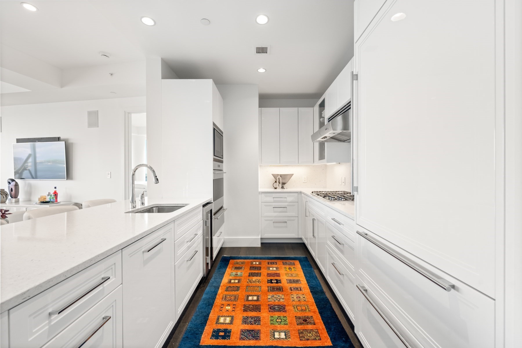White modern kitchen with quartz island, stainless steel appliances, and a colorful runner rug.