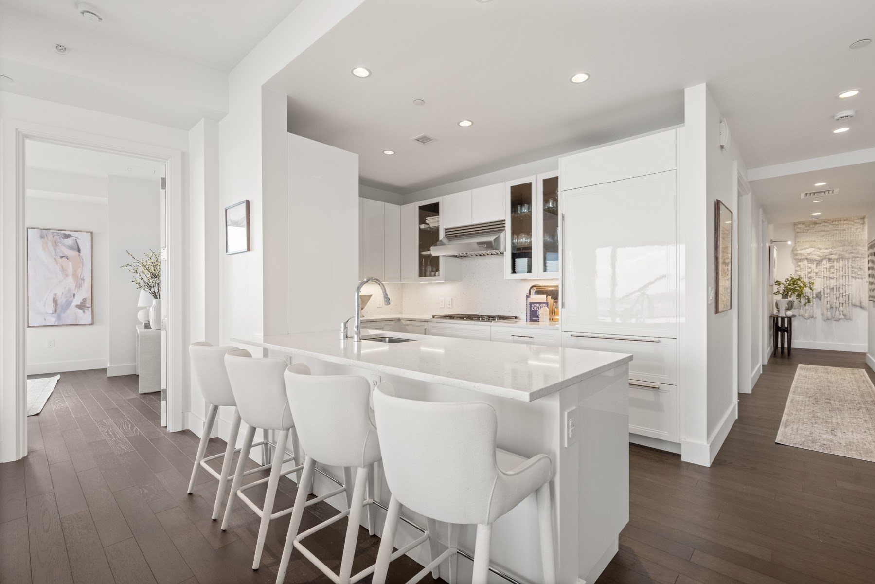 Modern white kitchen with a large island, four chairs, and dark wood floors.