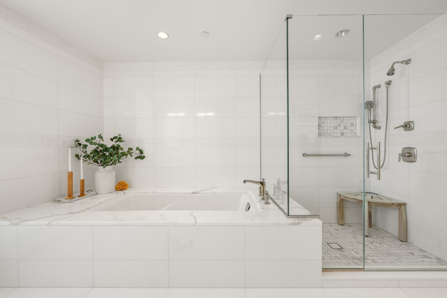 White-tiled bathroom with a marble-trimmed soaking tub and glass-enclosed shower.