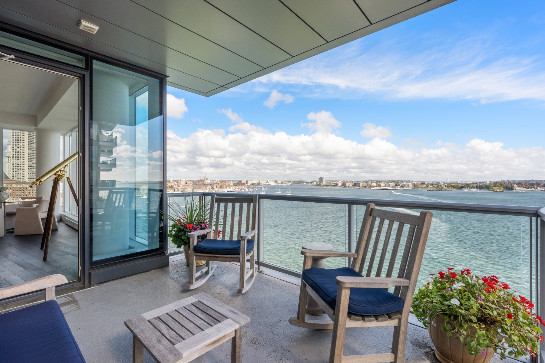 Furnished balcony overlooking the harbor, with wooden lounge chairs and potted flowers.