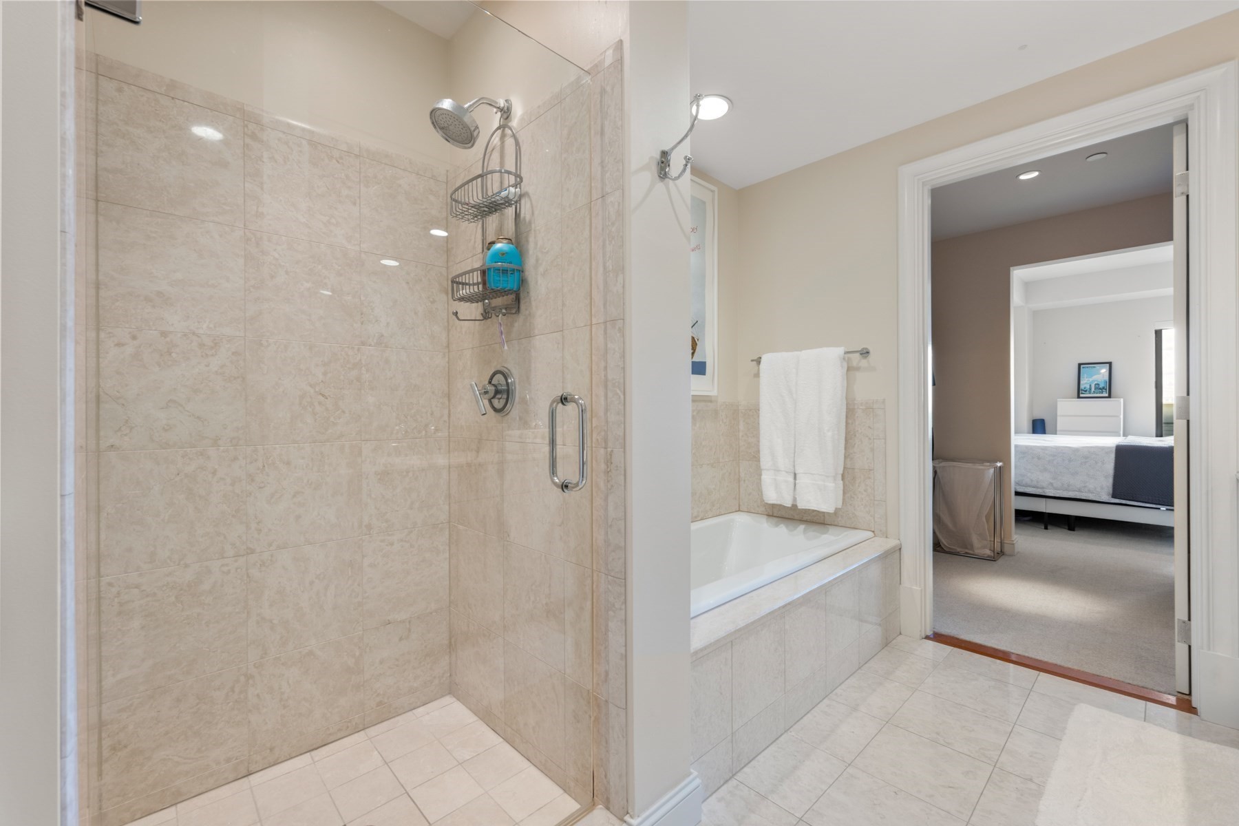 Tiled bathroom with a glass-enclosed shower and built-in tub beside an open doorway to a bedroom.