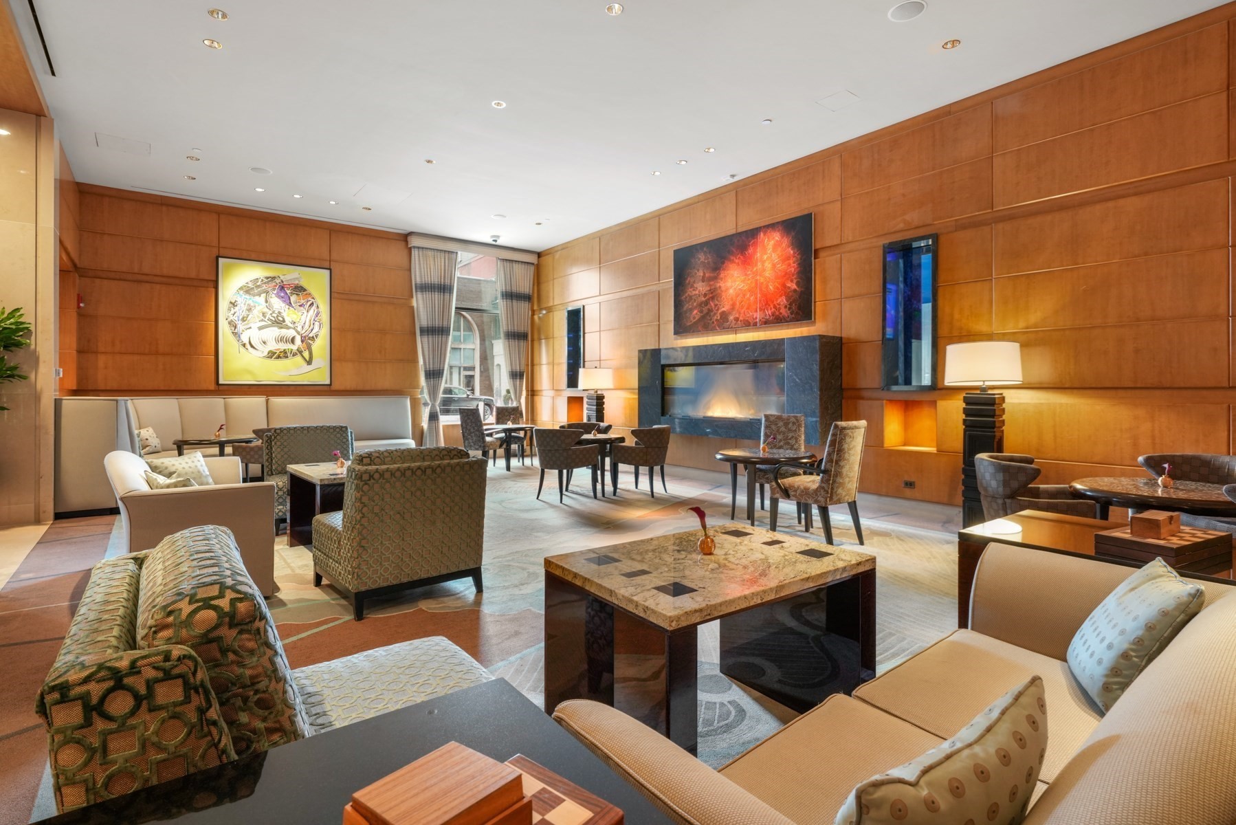 Furnished lounge with a fireplace, wood-paneled walls, and seating arranged around tables.